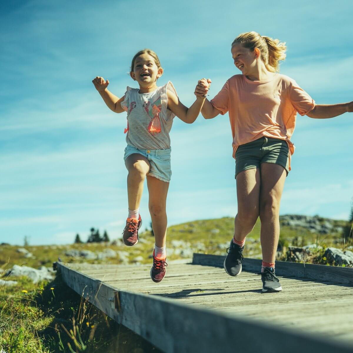 Zwei Mädchen laufen hüpfend und lachend auf dem barrierefreien Weg am Schöckl
