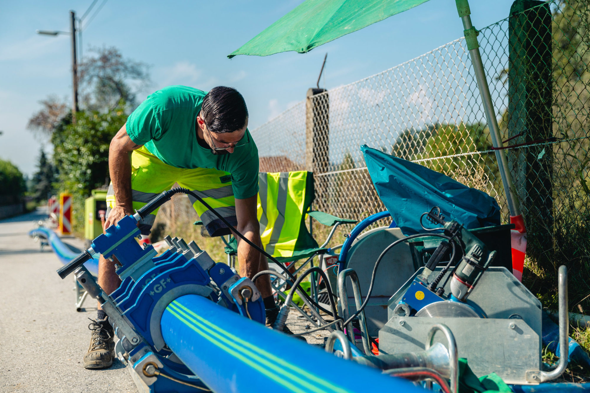 Arbeiter in sommerlicher Arbeitskleidung verbindet Wasserleitungsrohre an einer Baustelle