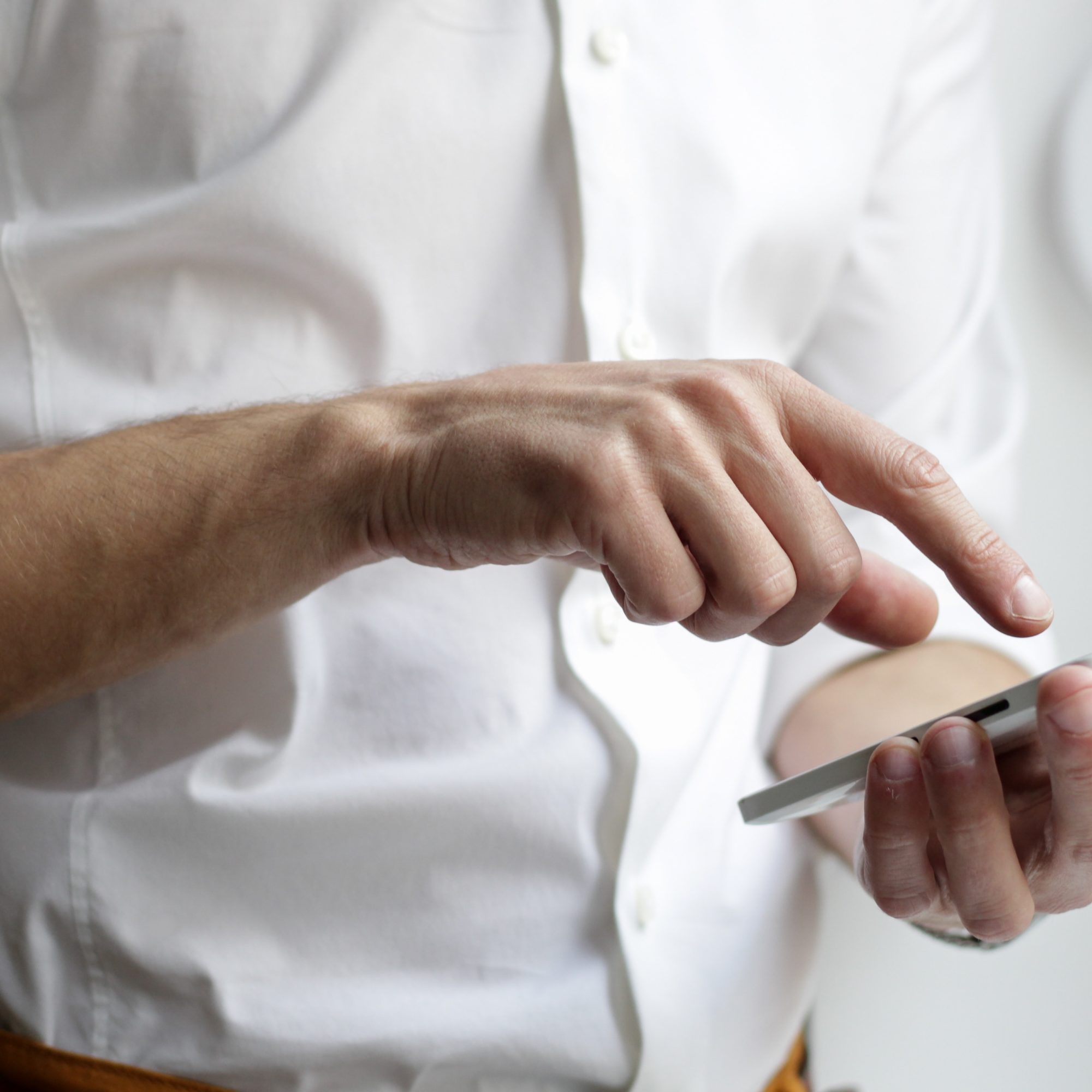 A man's hands are shown using a white smartphone. His index finger is pointing at the screen.
