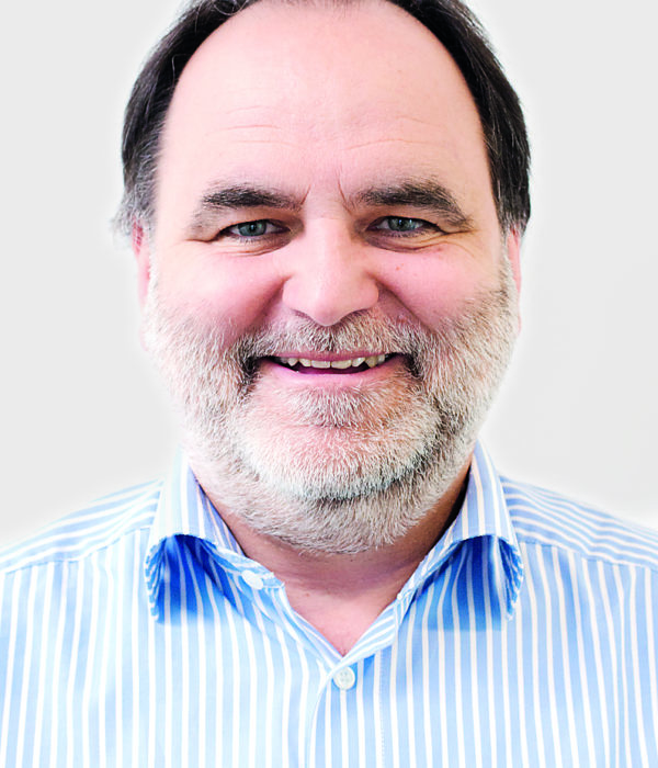 Headshot of Andreas Solymos, smiling and wearing a light blue striped shirt.