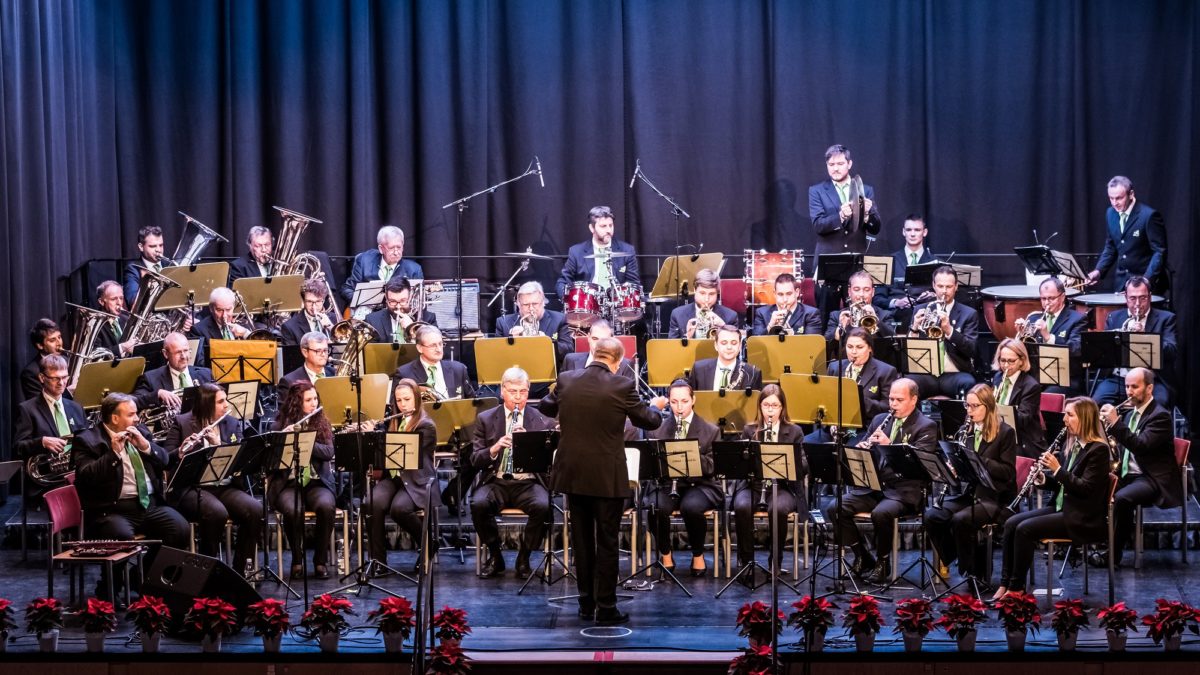 A large orchestra performs on stage, directed by a conductor in a black suit.