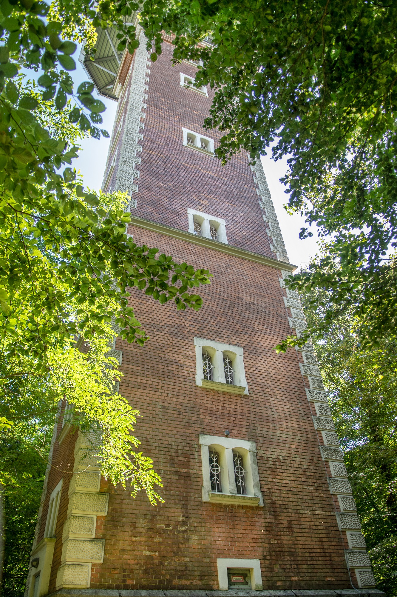 A brick tower with several windows, seen from a low angle through trees. The tower is called the Hilmwarte