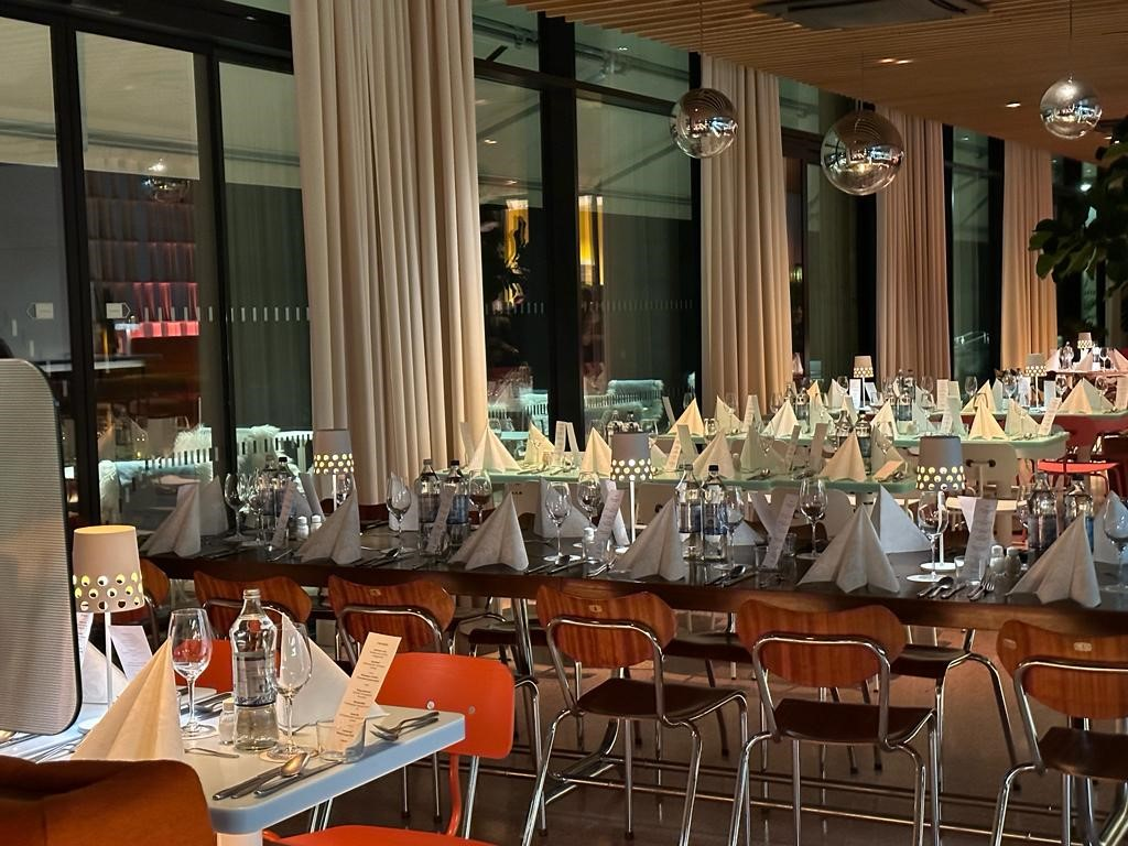 Festlich gedeckter Speisesaal mit weißer Tischdekoration, Gläsern und Lampen in elegantem Ambiente.