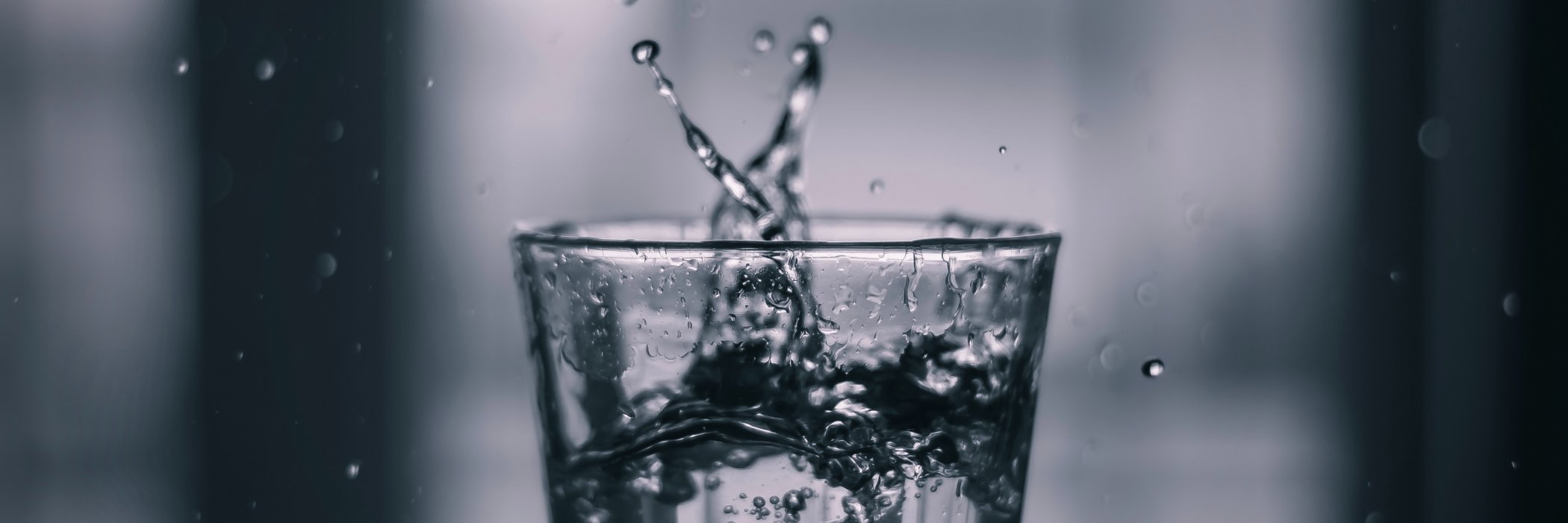 Schwarz-weiß-Foto eines Glases, in das Wasser spritzt, mit Tropfen in der Luft eingefangen