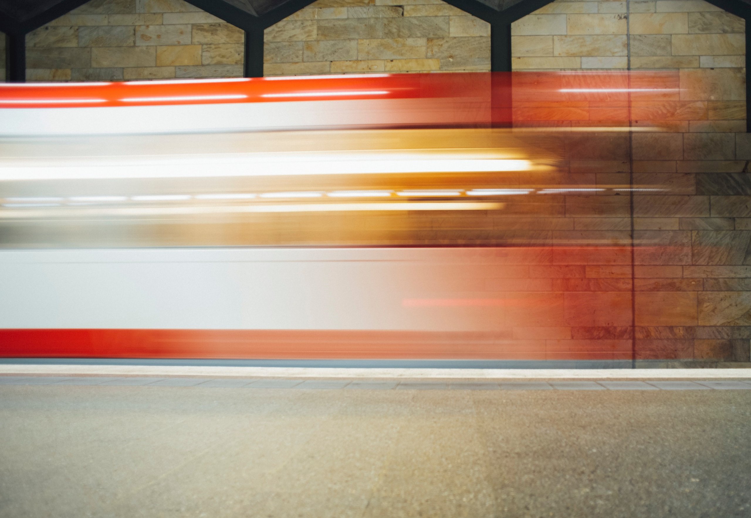 A red and white train speeds past a brick wall.