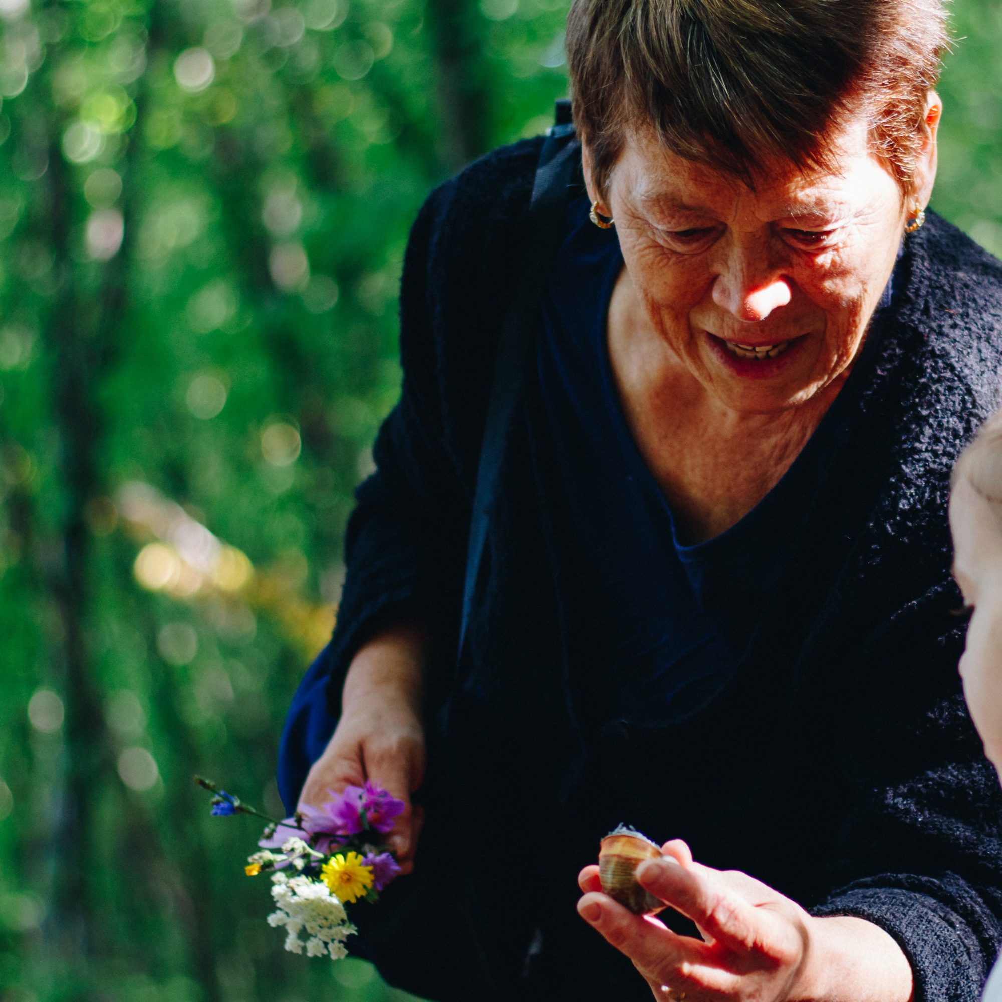 Ältere Dame hält Schneckenhaus in der Hand und zeigt es jungem Mädchen