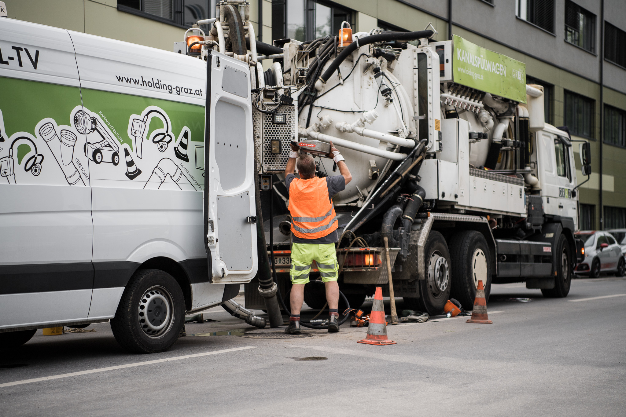 Arbeiter mit Warnweste bedient einen Kanalspülwagen auf einer Straße, daneben steht kanal-TV-Fahrzeug