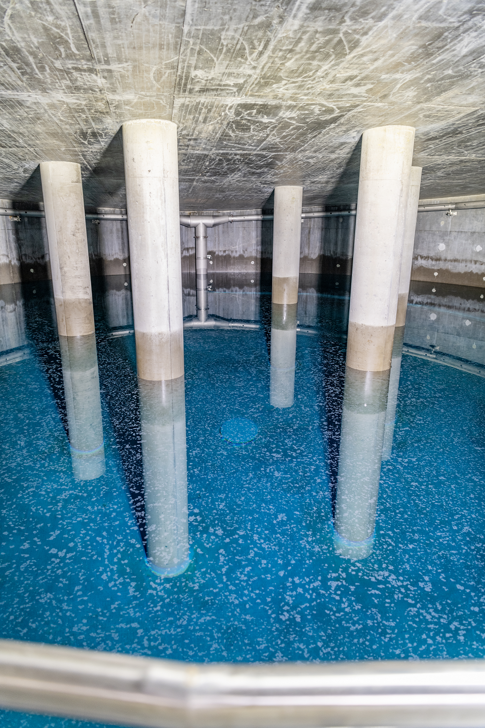 Innenansicht eines Hochbehälters mit Betonpfeilern und blauem Wasser.
