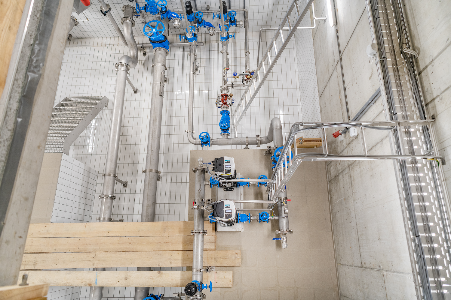 Technikraum mit Rohren, Ventilen und blauen Armaturen für die Wasserversorgung.