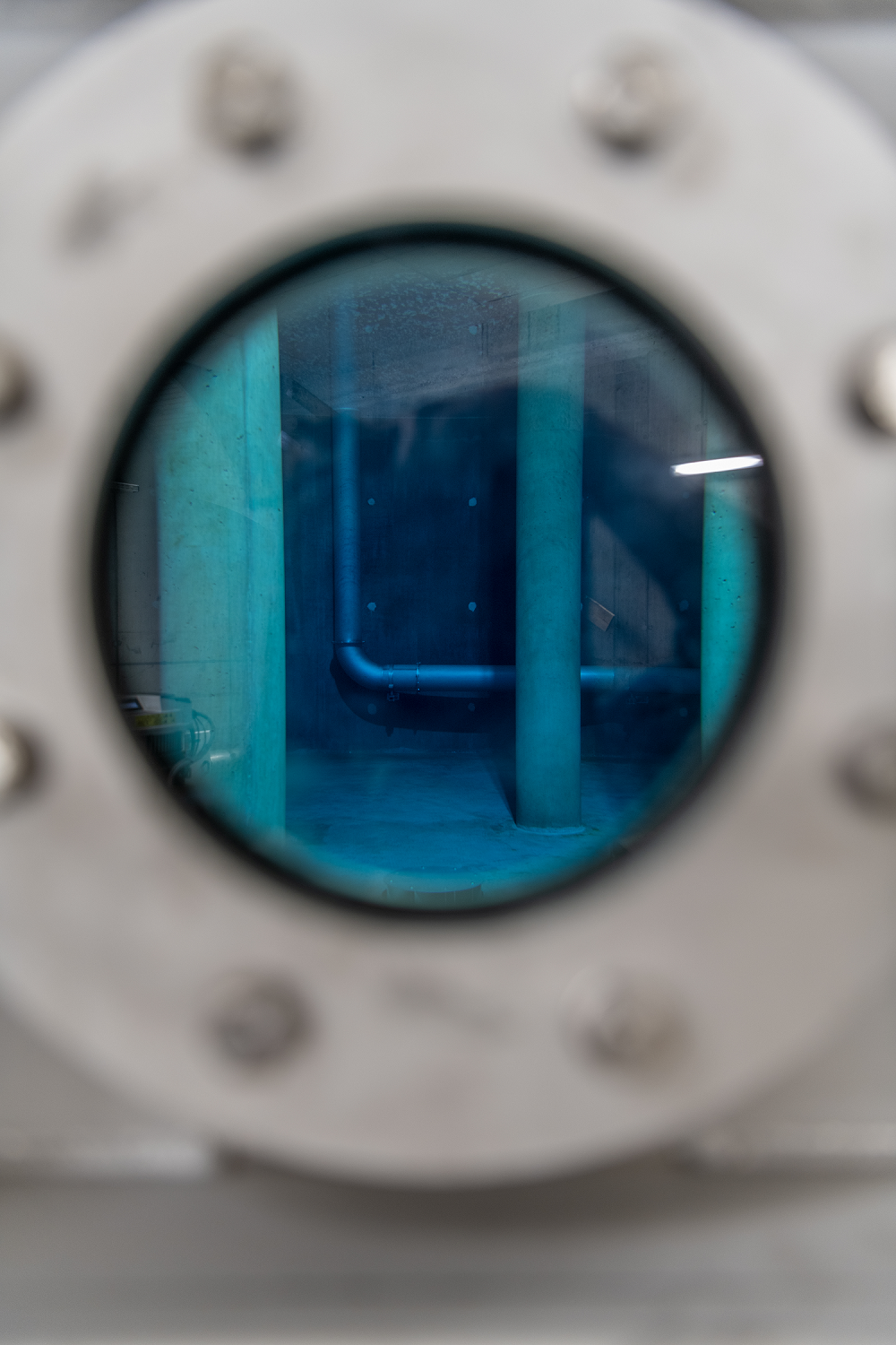 Blick durch ein rundes Fenster auf einen Wasserbehälter mit Säulen und Rohrleitungen