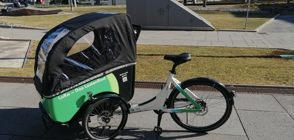 Ein weißes Lastenrad mit grünem Korb und der Aufschrift "LaRa – Das LastenRad".