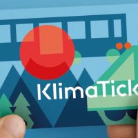 Hand hält bunte KlimaTicket-Karte mit grafischen Elementen wie Bäumen, Bahn und Person.