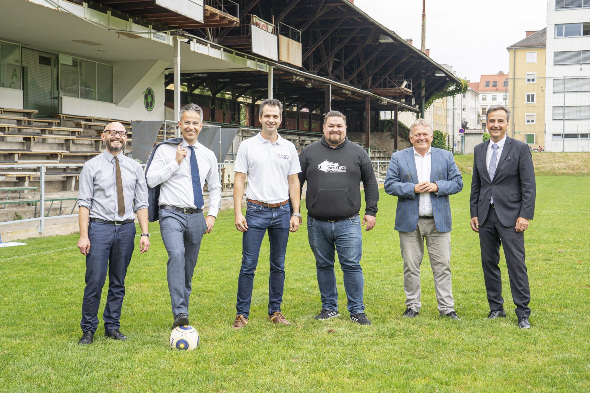 Mehrere Personen stehen auf dem Rasen der Gruabn, im Hintergrund historische Holztribüne.