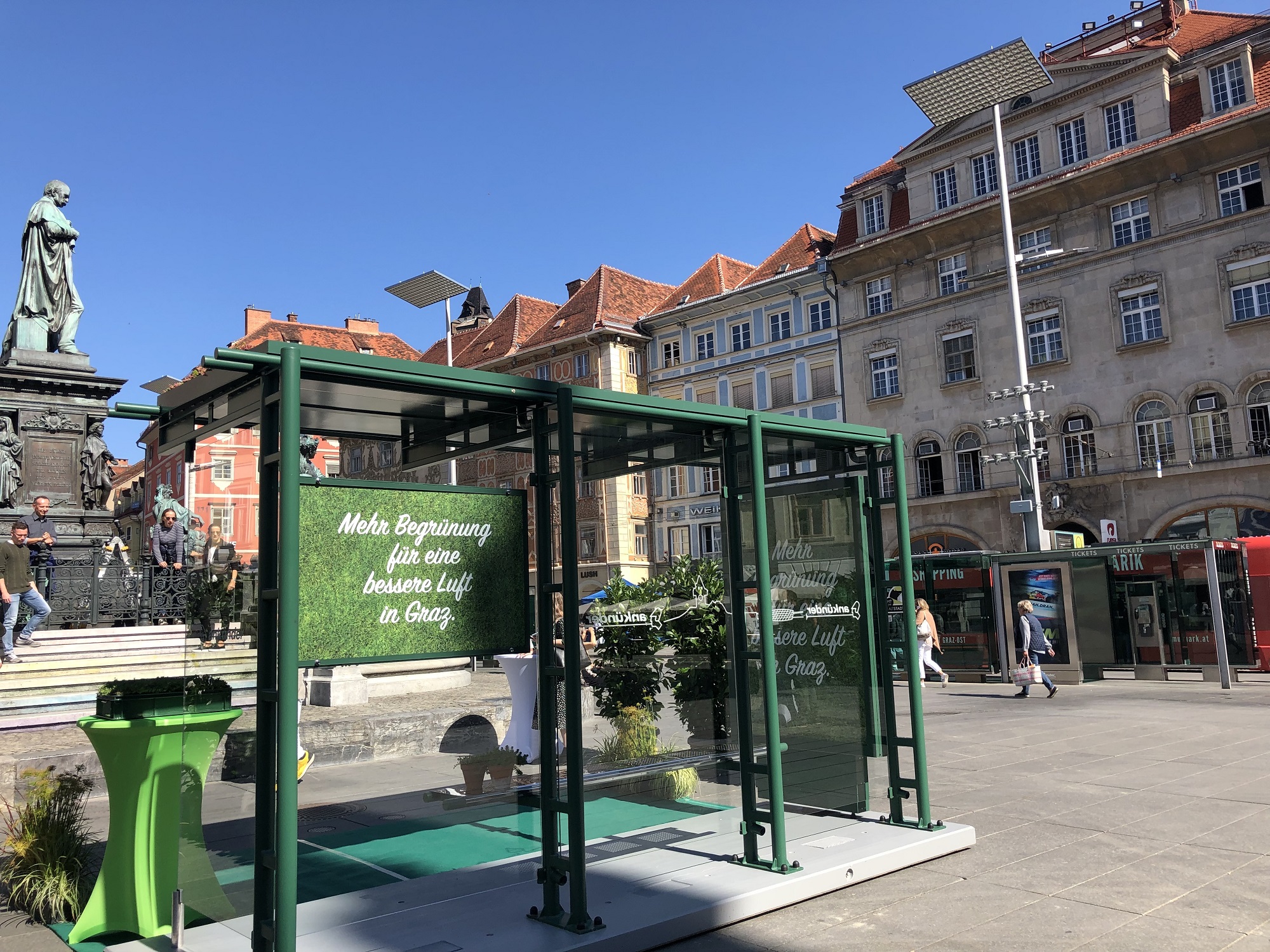 Begrüntes Wartehäuschen mit Aufschrift "Mehr Begrünung für eine bessere Luft in Graz" am Hauptplatz.