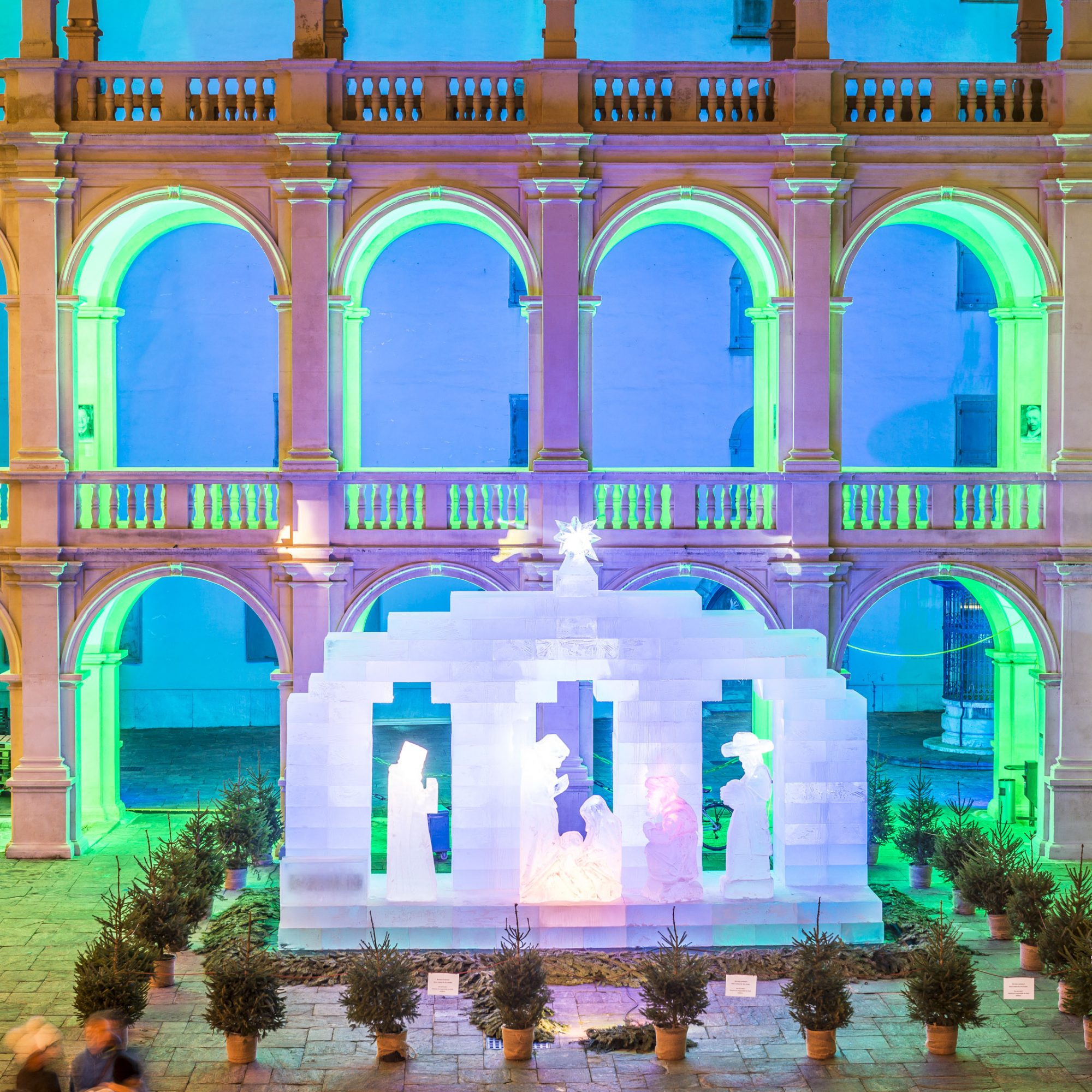 Blick auf die hell erleuchtete Eiskrippe im Landhaushof. Sie ist umringt von kleinen Tannenbäumen.