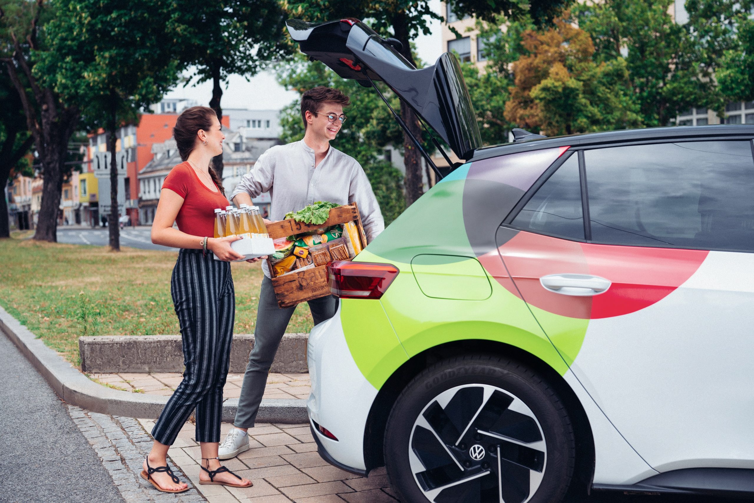 Junges Paar lädt Lebensmittel und Palette Makava-Eistee in den Kofferraum eines tim-Autos.