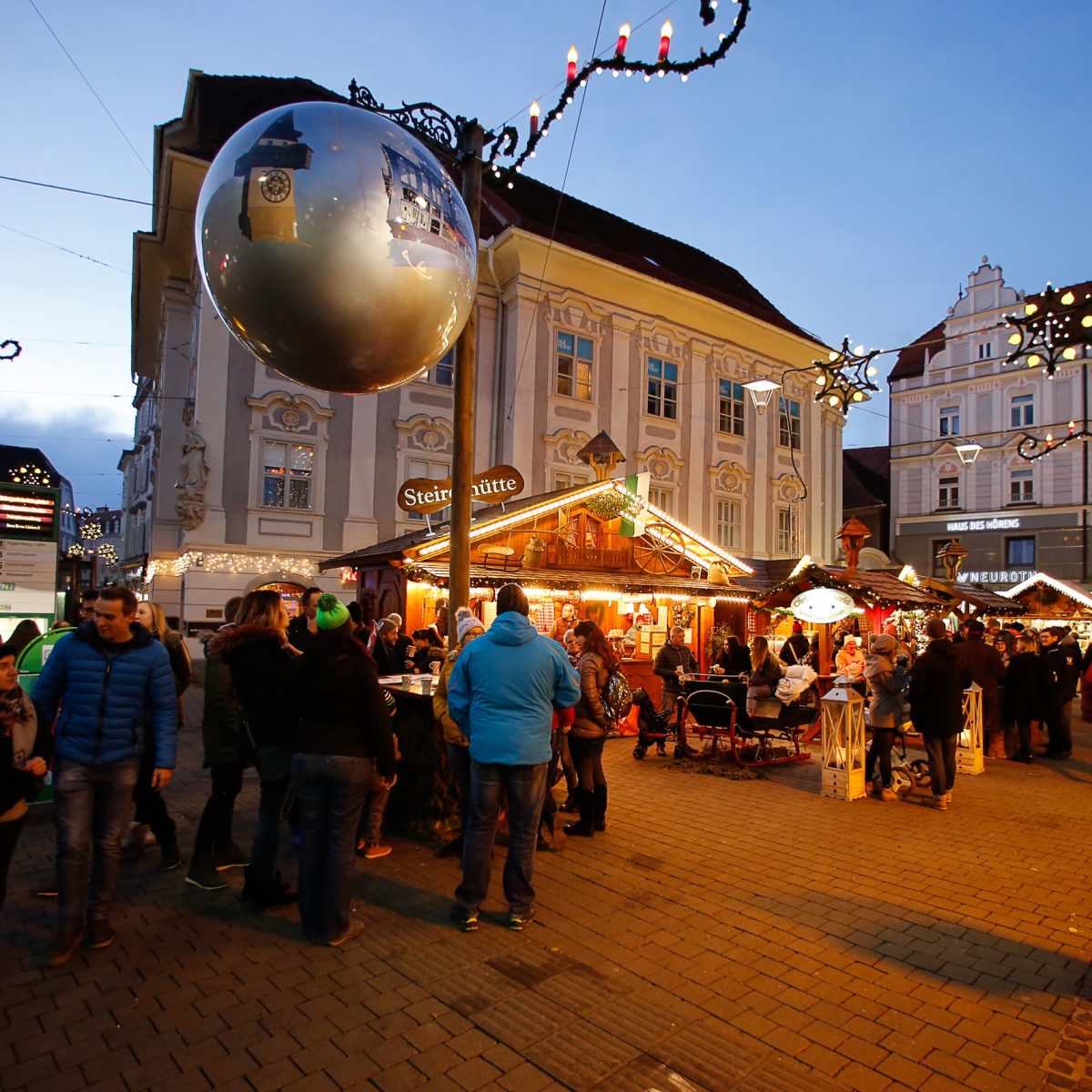 Südtirolerplatz in Graz mit beleuchtetem Weihnachtsmarkt und vielen Besucher:innen