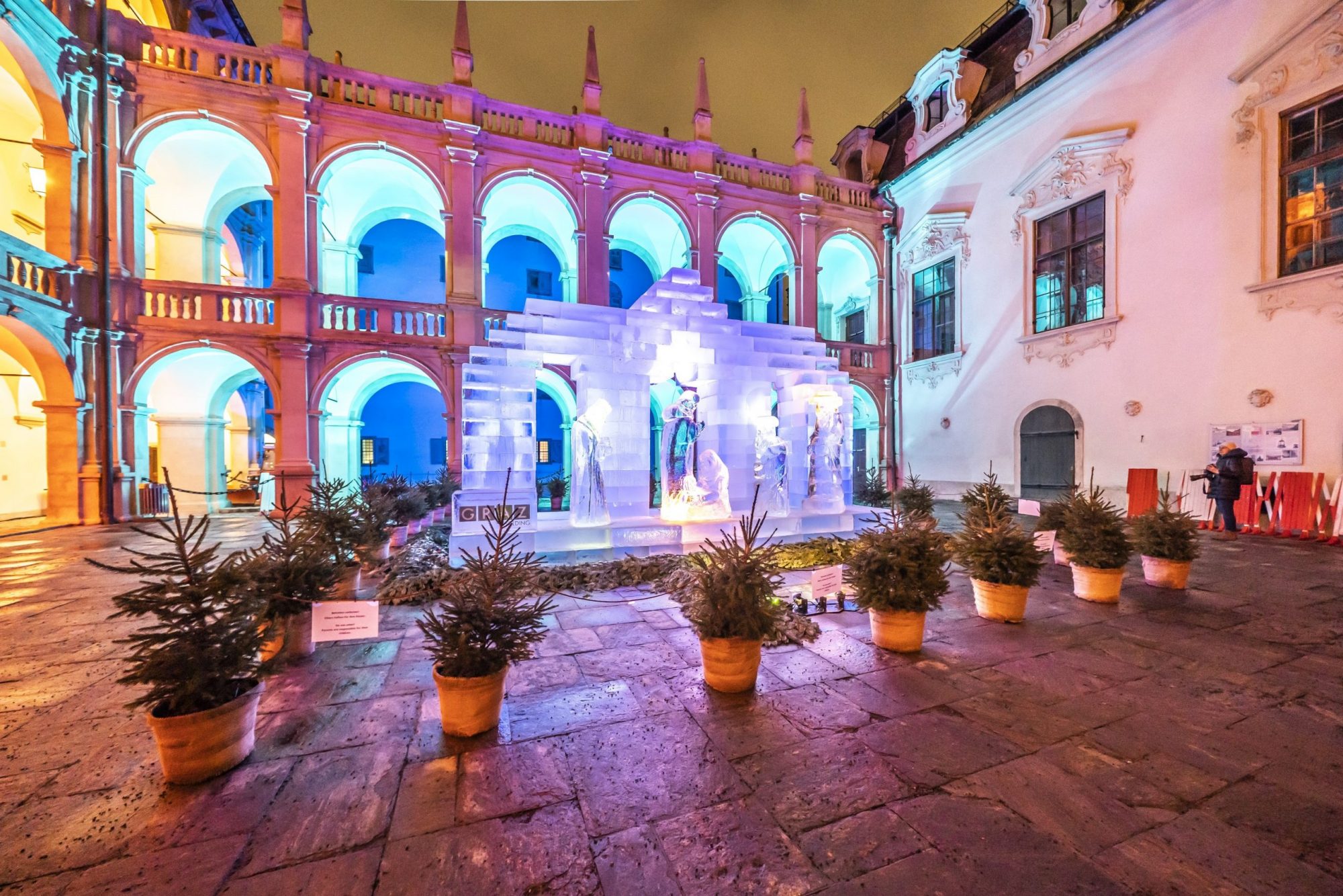 Eiskrippe im Landhaushof mit bunter Beleuchtung und barocken Gebäudebögen im Hintergrund.