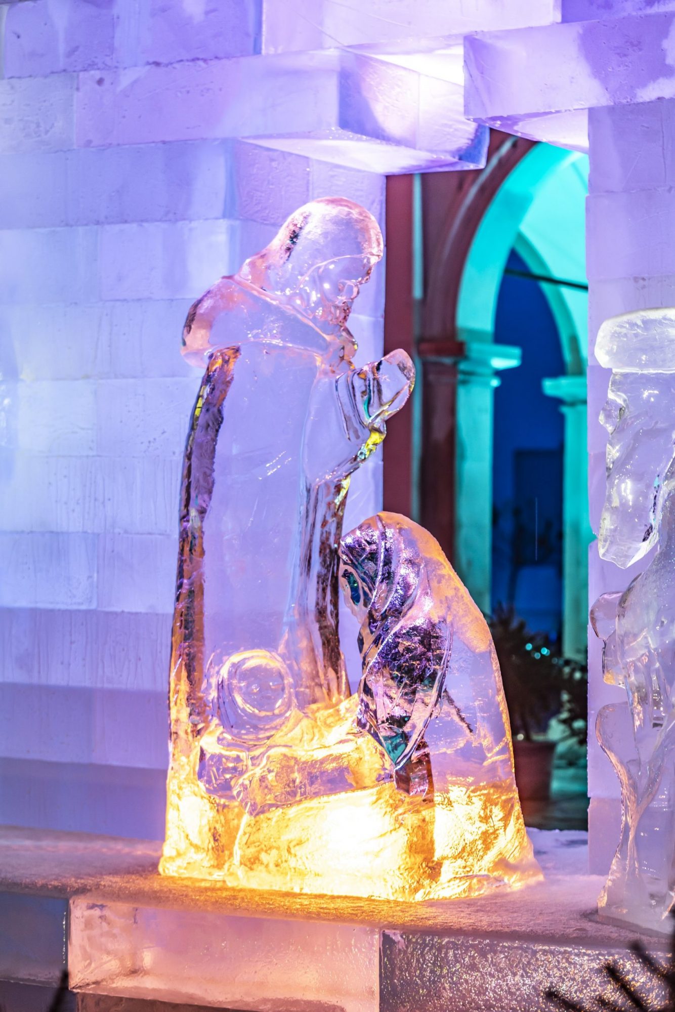 Detailaufnahme einer beleuchteten Eiskrippenfigur mit Maria und Josef im farbig erleuchteten Landhaushof.