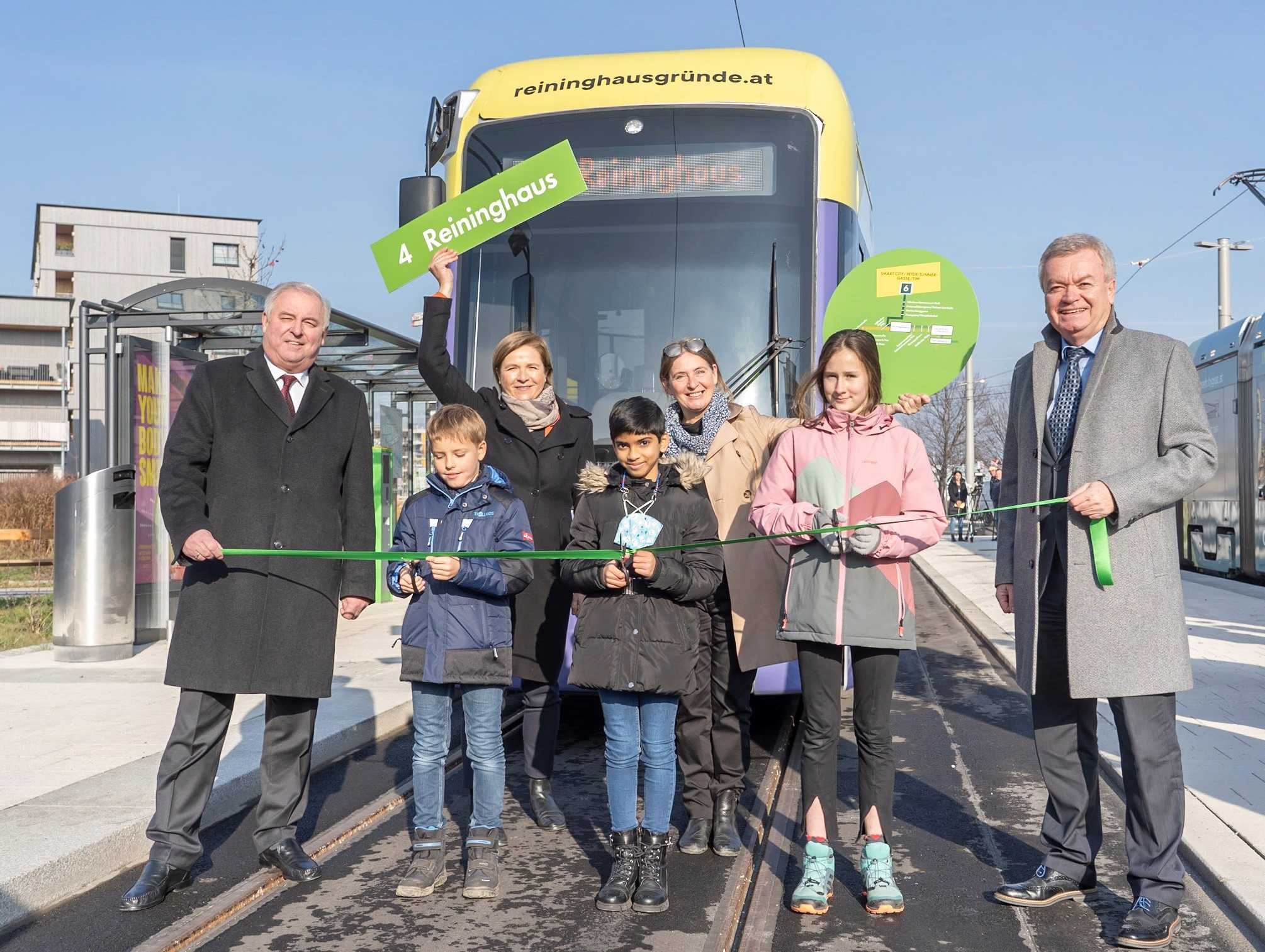 Eröffnung der Straßenbahnverlängerung in Graz mit Menschen, zwei Bahnen und Schildern der Linien 4.