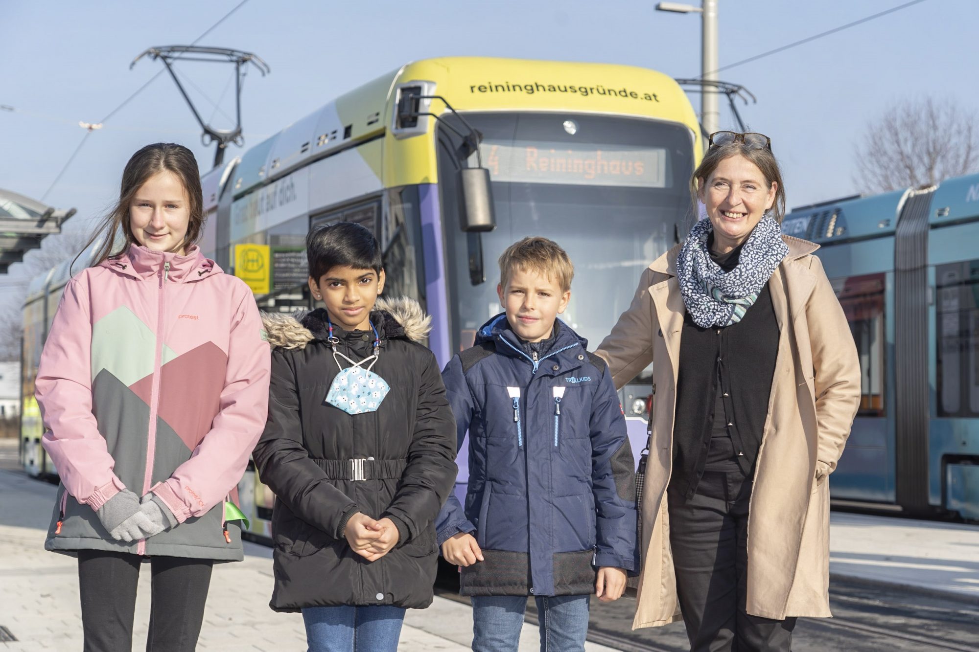 Drei Kinder und Bürgermeisterin Elke Kahr vor einer Straßenbahngarnitur der Linie 4.
