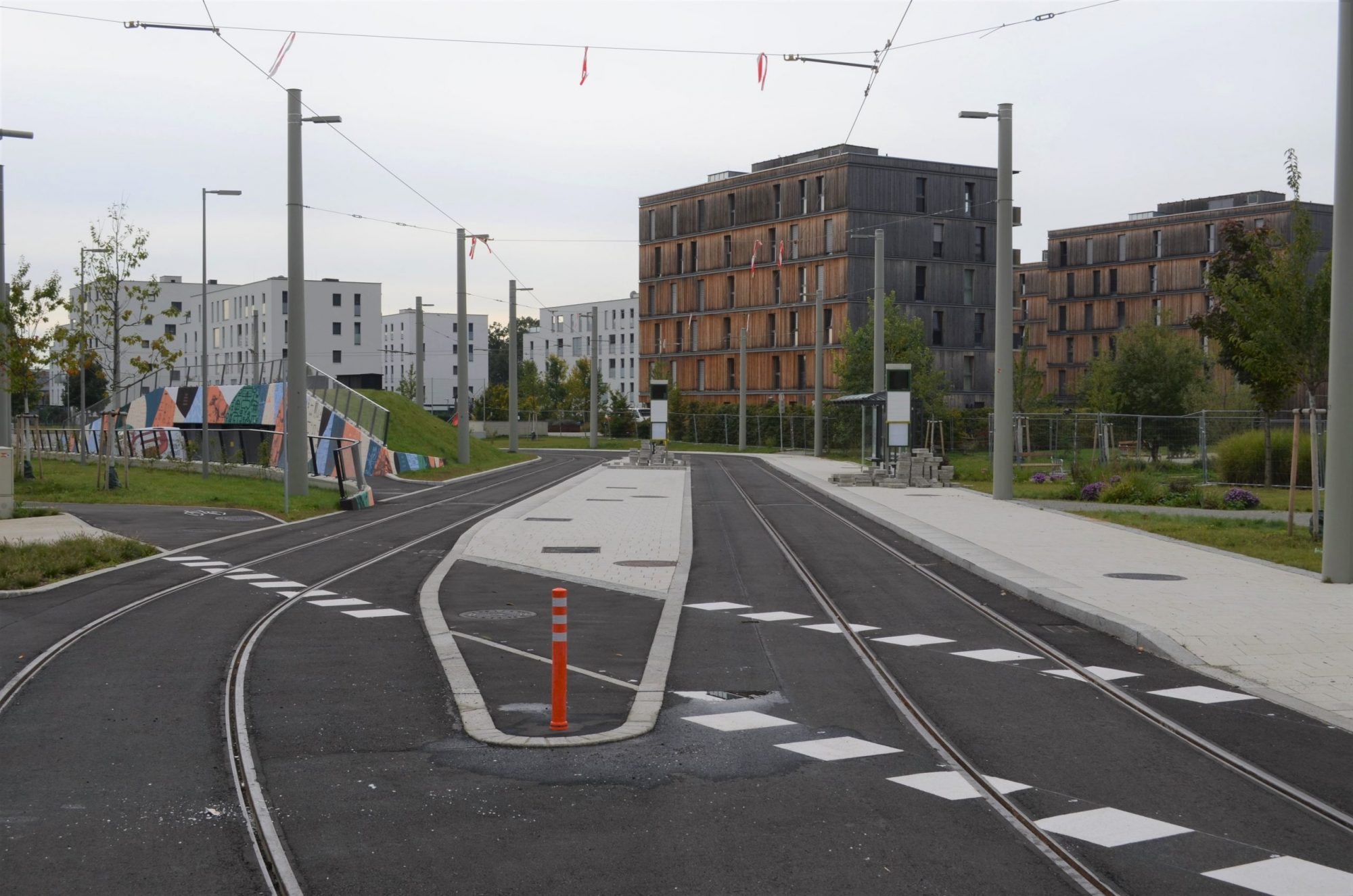 Neue Straßenbahnhaltestelle in modernem Wohngebiet mit Gleisen, Wartebereich und umliegenden Gebäuden