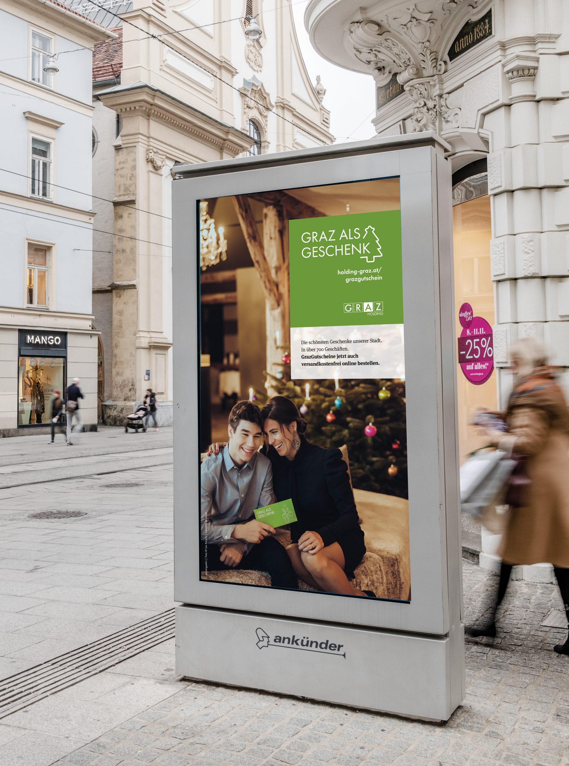 Werbung für GrazGutscheine mit Slogan "Graz als Geschenk" auf beleuchteter Infotafel in Herrengasse.