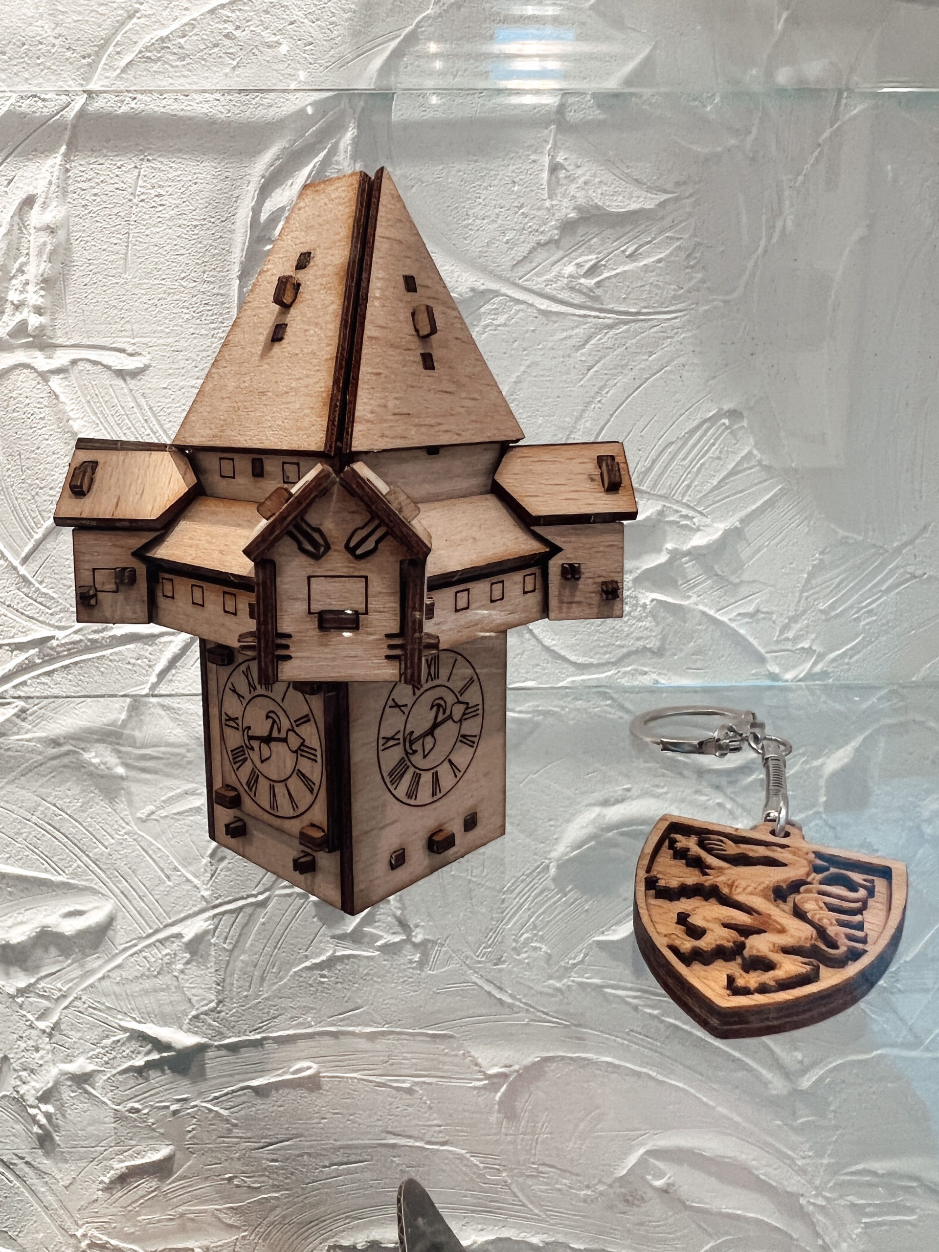 Uhrturm aus Holz und Schlüsselanhänger mit steirischem Panther aus Holz nebeneinander in einem Schaufenster