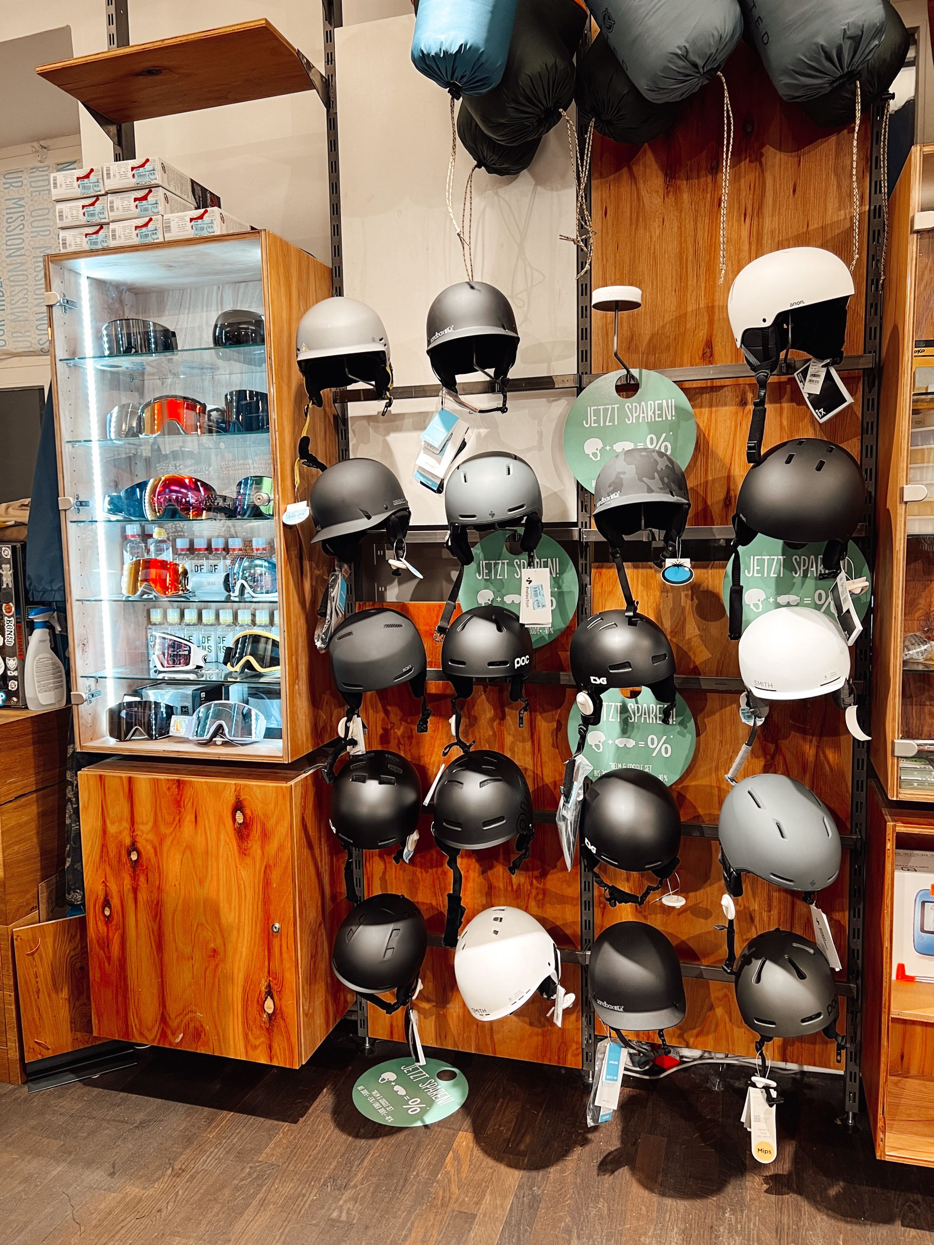verschiedenen Helme an einer Wand, daneben ein Schrank mit Beleuchtung und verschiedenen Ski- und Snowboard-Brillen in einem Geschäft