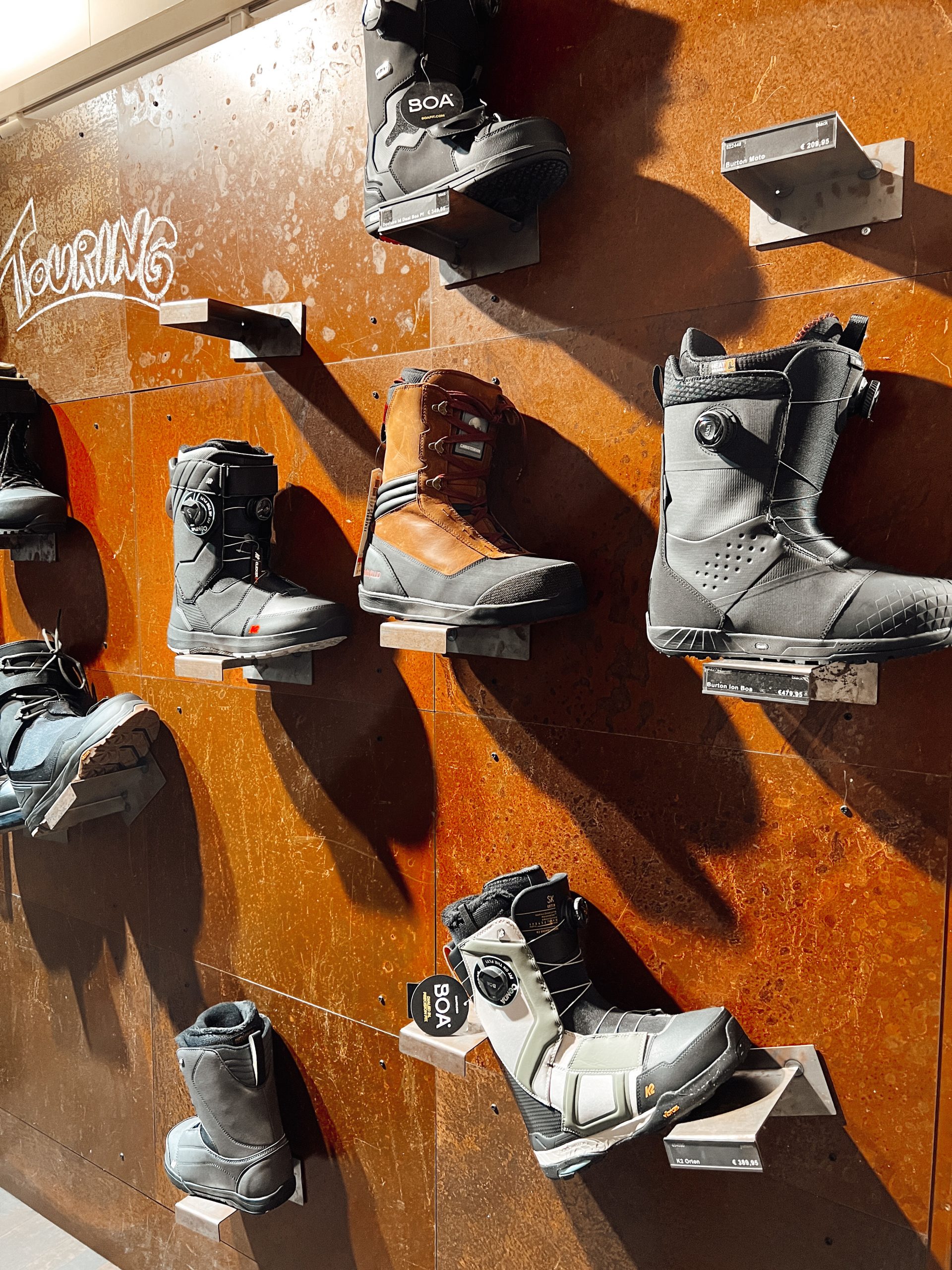 verschiedene Schuhe (Snowboard, Winterstiefel) auf Halterungen an der Wand eines Geschäfts