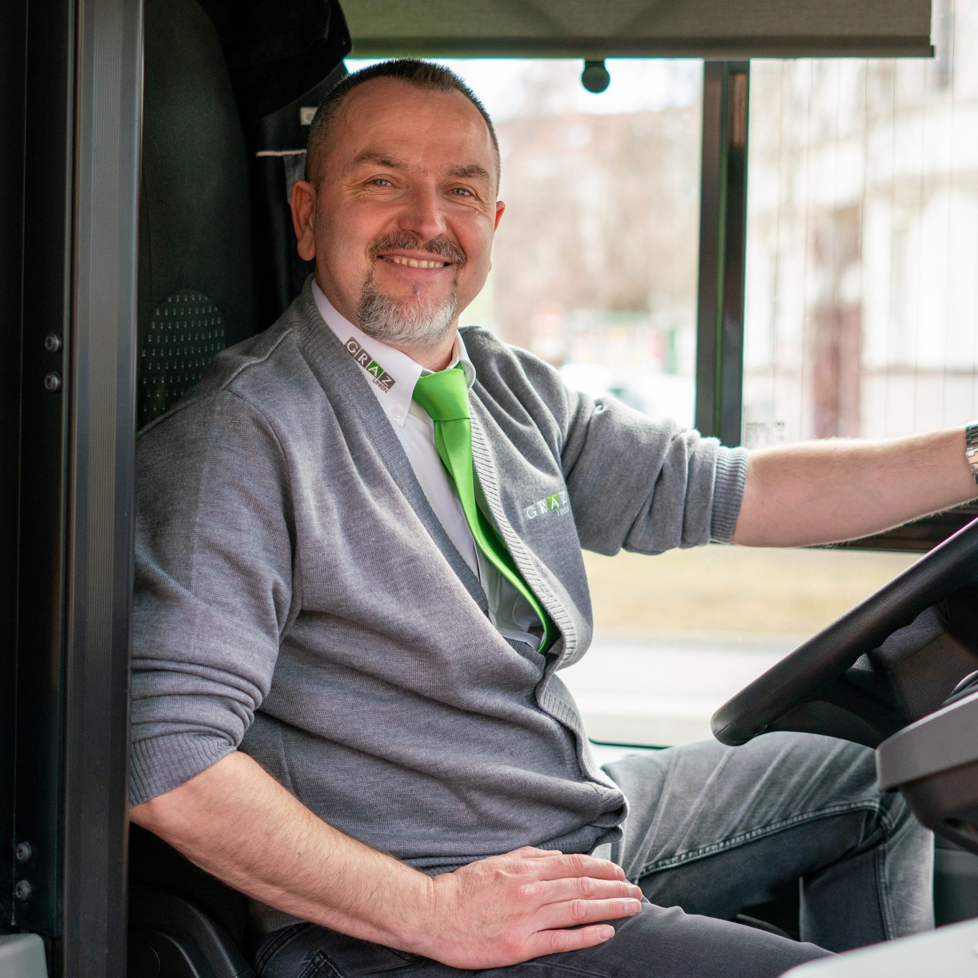 Latifaj Nexhat, a bus driver for Graz Linien, smiles at the camera while sitting at the wheel.