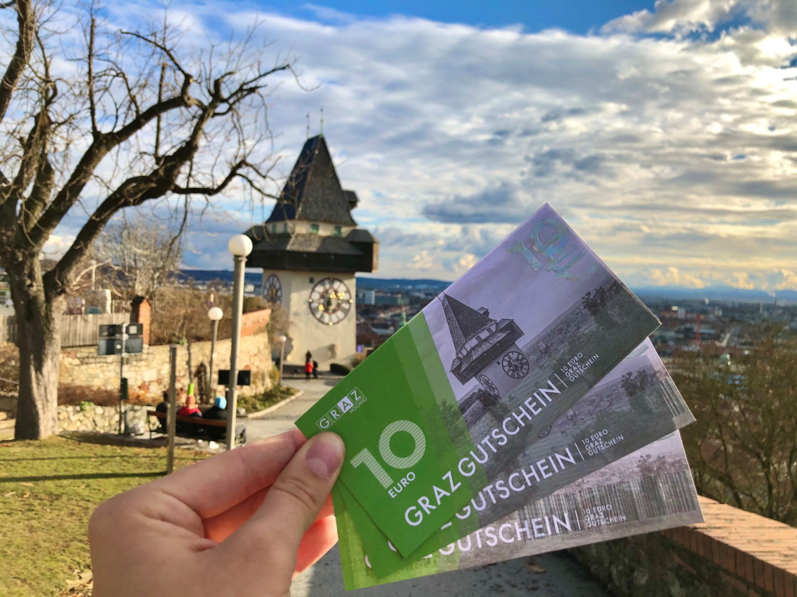 GrazGutschein in einer Hand vor dem Uhrturm