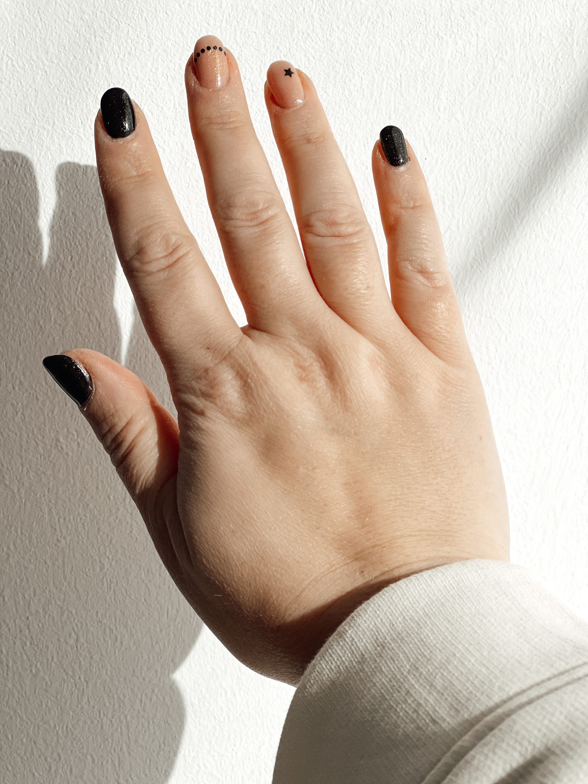 Hand mit Nagellack und -verzierungen vor einer weißen Wand