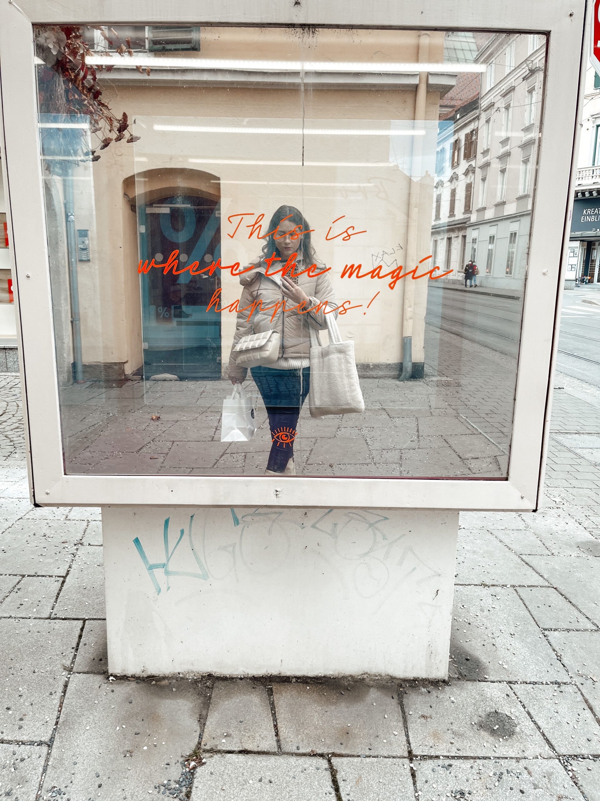 junge Frau macht ein Spiegelfoto in einem Spiegel vor dem Studio "Augenweide" mit der Aufschrift "This is where the magic happens!"