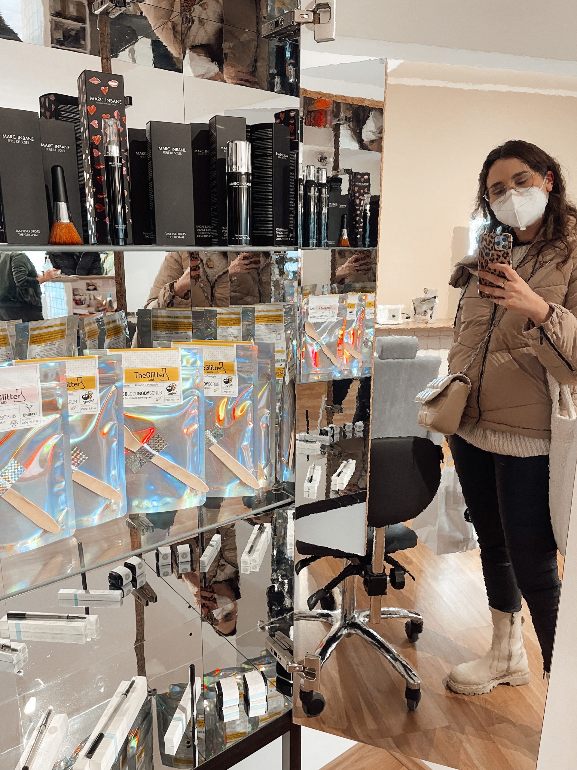 junge Frau macht ein Spiegelfoto neben einem Regal mit Beauty-Produkten