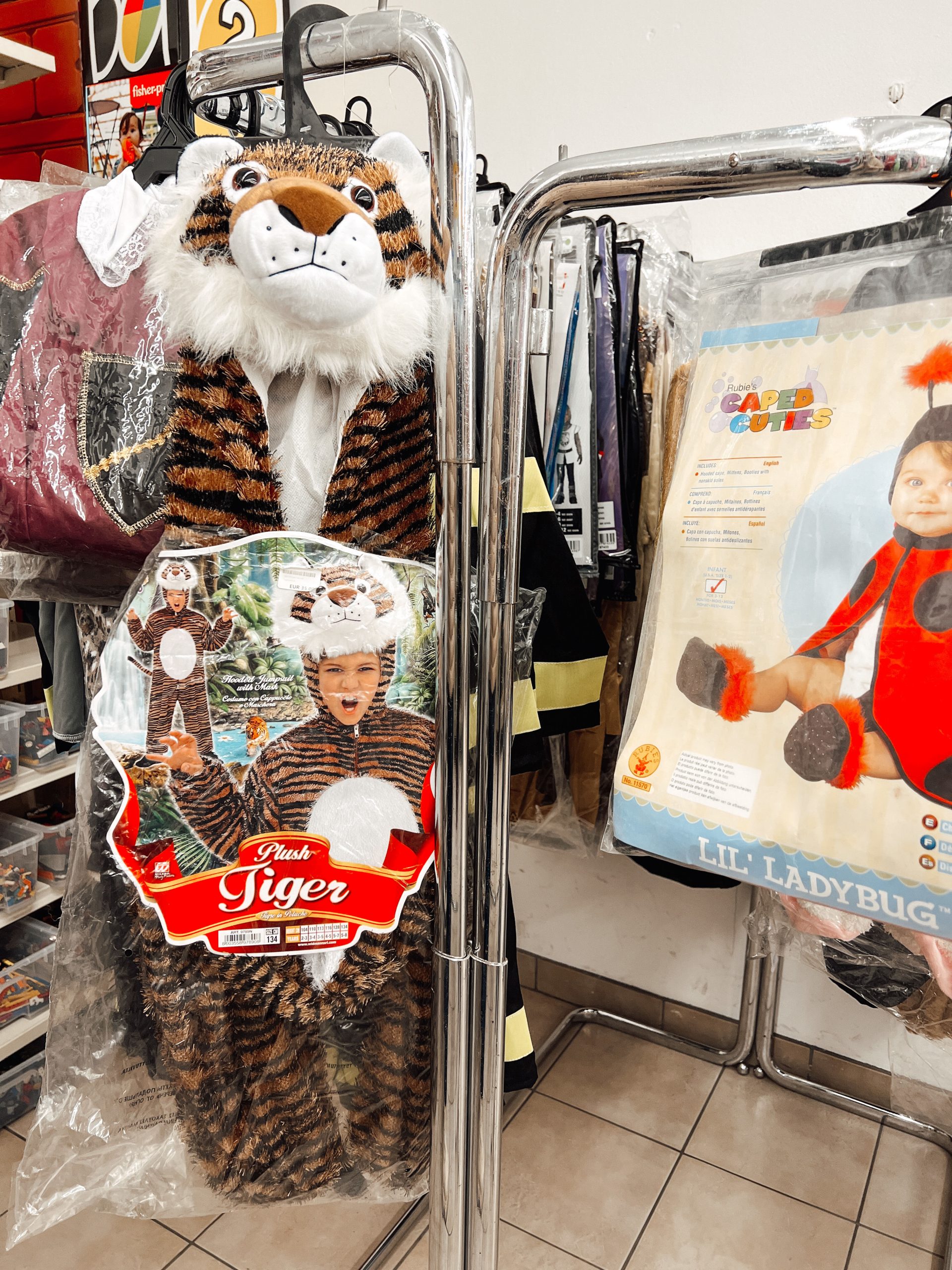 verschiedene Kostüme wie Tigerkostüm und Marienkäferkostüm für Kinder auf einem Kleiderständer in einem Geschäft