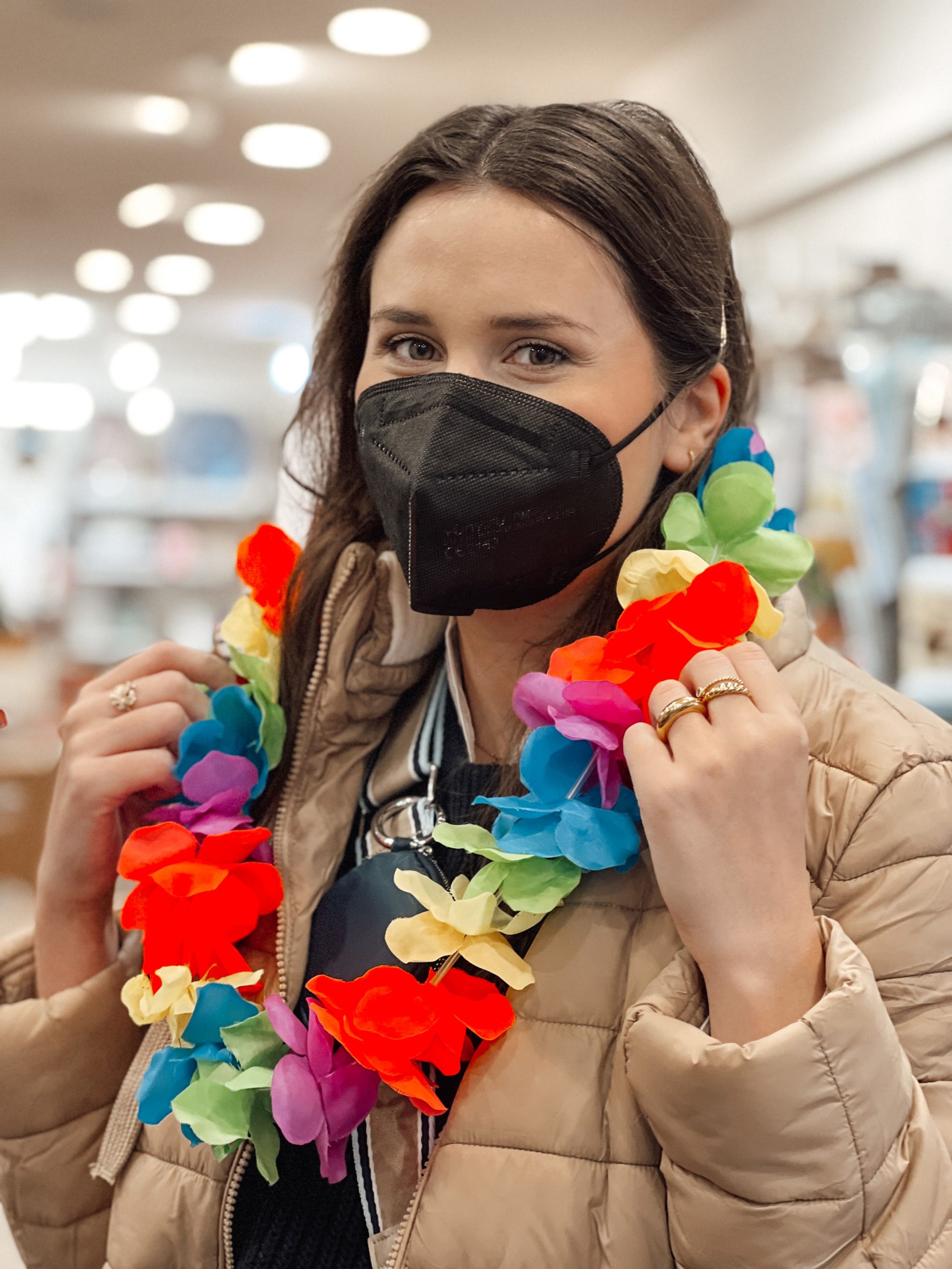 junge Frau mit schwarzer FFP-2-Maske und Blumenkette in einem Geschäft