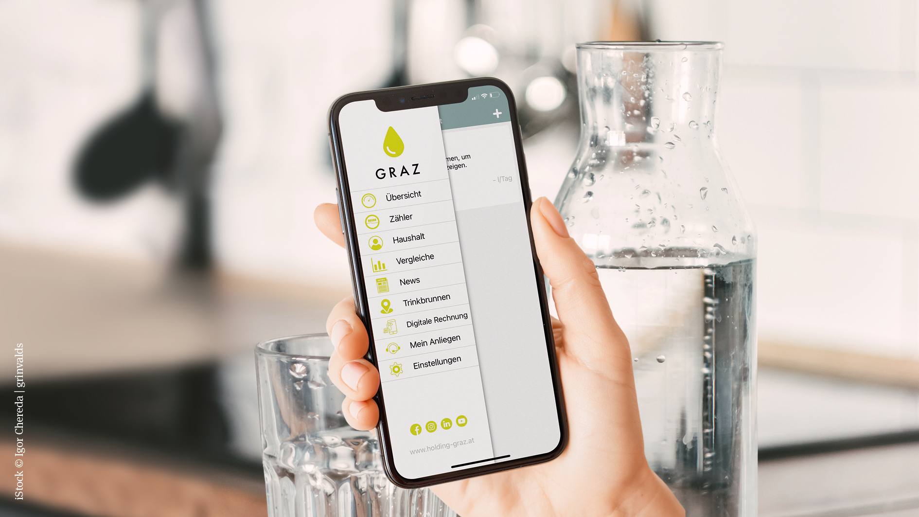 Hand hält Smartphone mit geöffneter Graz Wasser-App, dahinter Wasserkrug