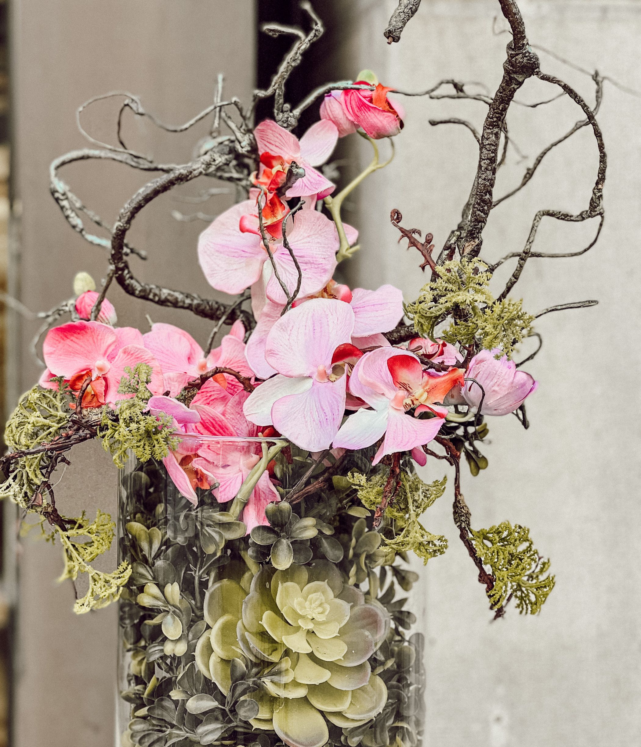 Blumengesteck in einer Vase mit rosa Orchideen, Zweigen, Moos und Buchszweigen