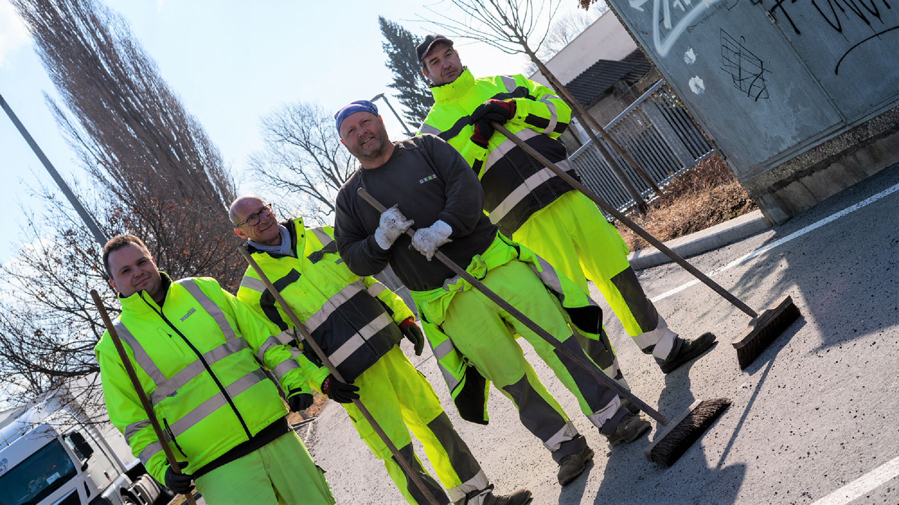 Vier Mitarbeiter des Stadtraumes in Arbeitskleidung und mit Besen stehen nebeneinander.