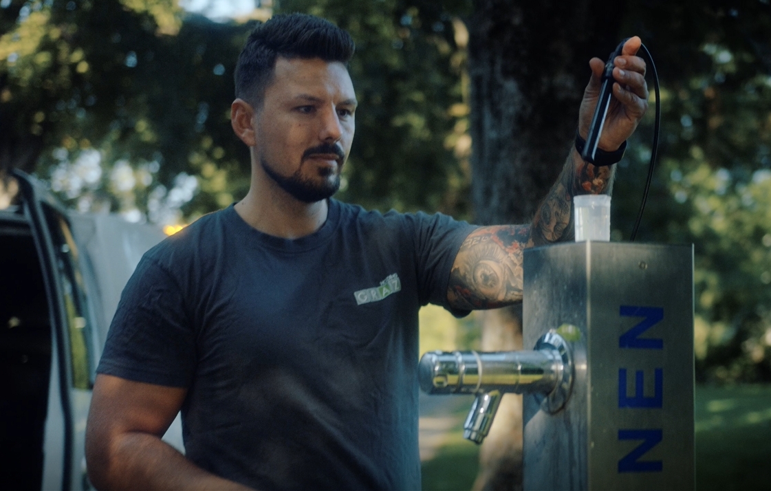 Tätowierter Mitarbeiter der Holding Graz-Wasserwirtschaft prüft Funktion eines Trinkbrunnens