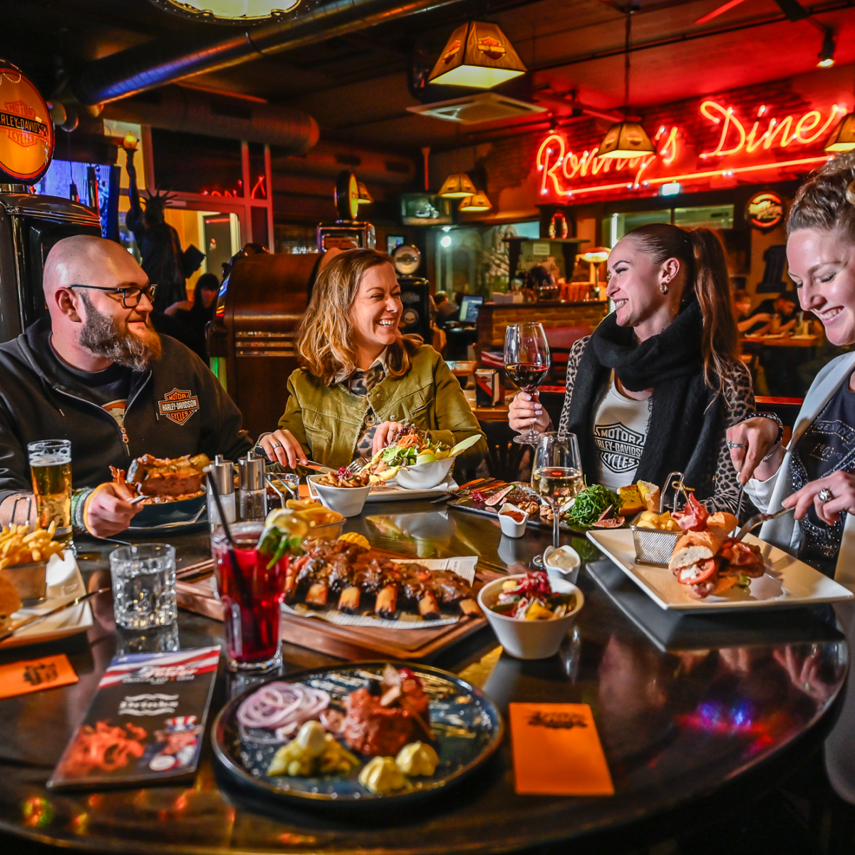 Vier Freunde beim Essen im "Ronny's Diner" in Graz; Neonreklame.