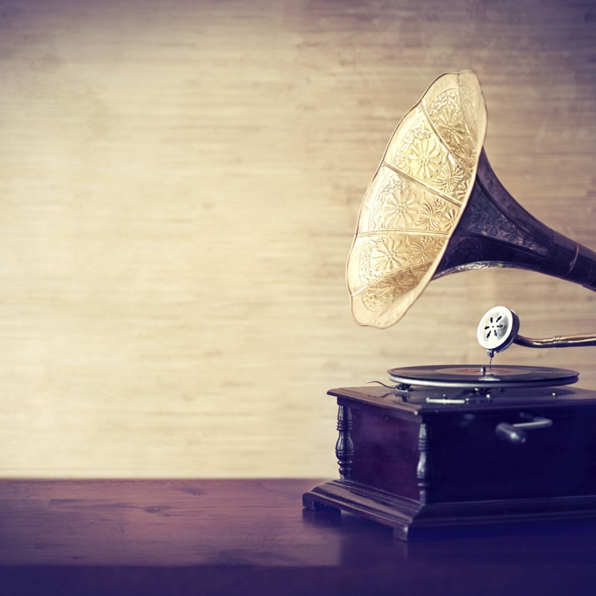 Antikes Grammophon mit verziertem Trichter auf Holztisch vor einer beige strukturierten Wand.