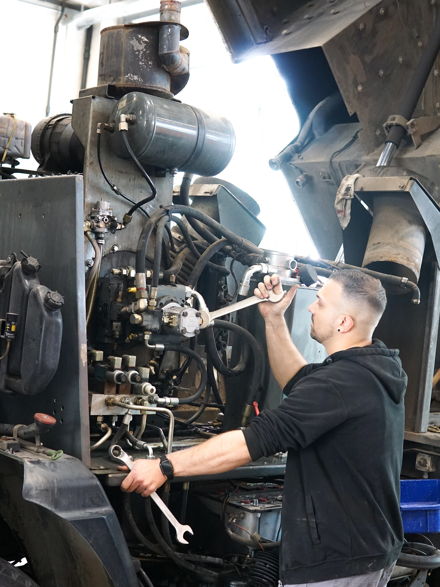 Mann repariert mit Werkzeug große Maschine in Werkstatt, um ihn technische Teile