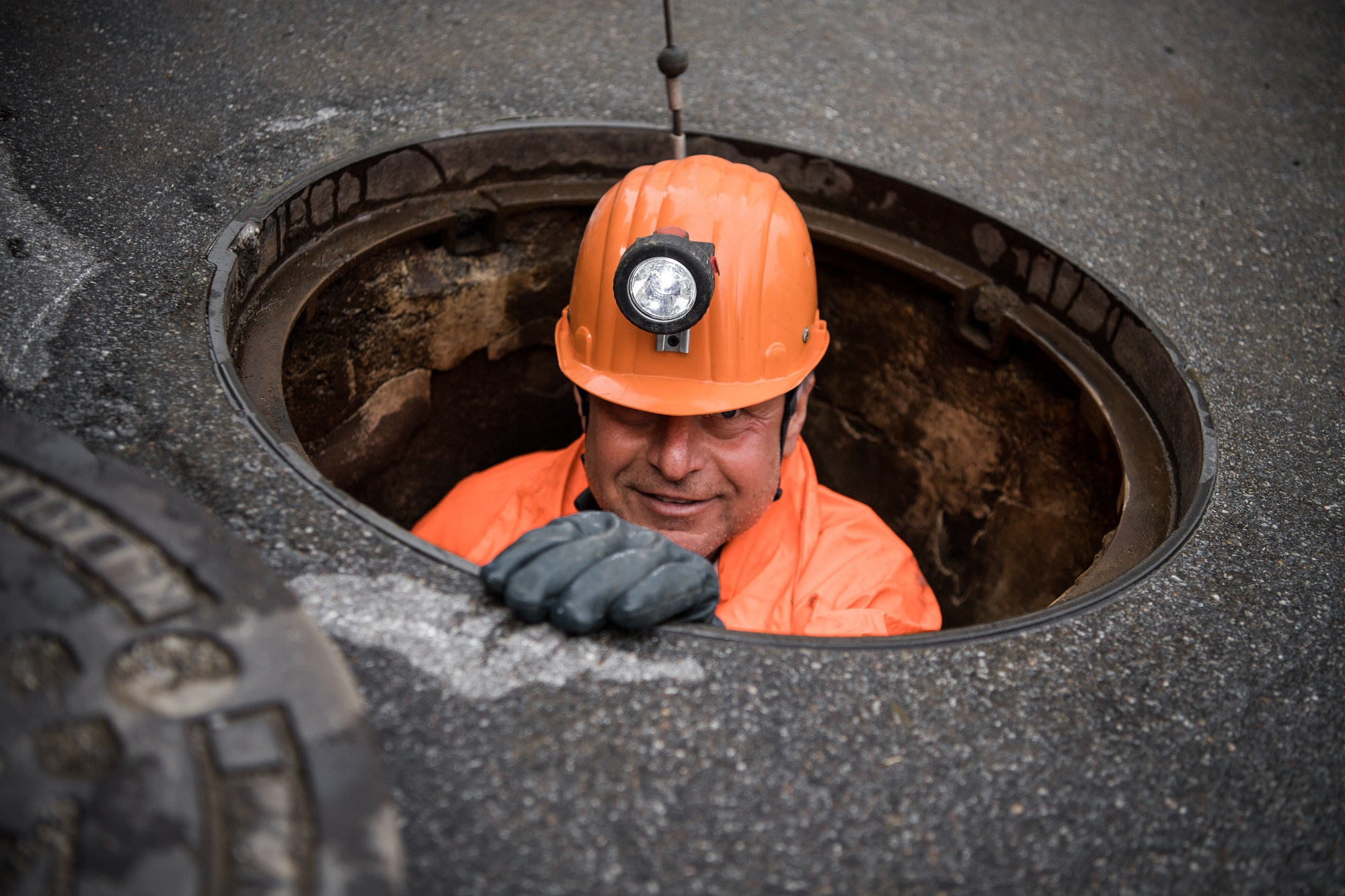 Arbeiter mit Helm und Stirnlampe steigt aus Kanaldeckel