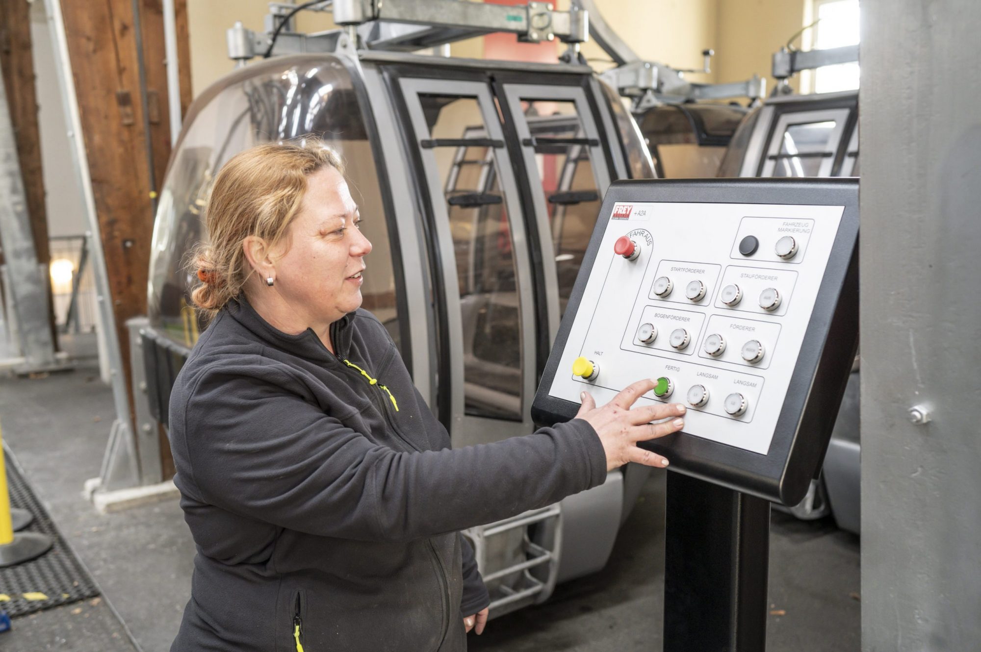 Eine Frau bedient ein Steuerpult vor Gondeln der Schöckl-Seilbahn in einer Station.