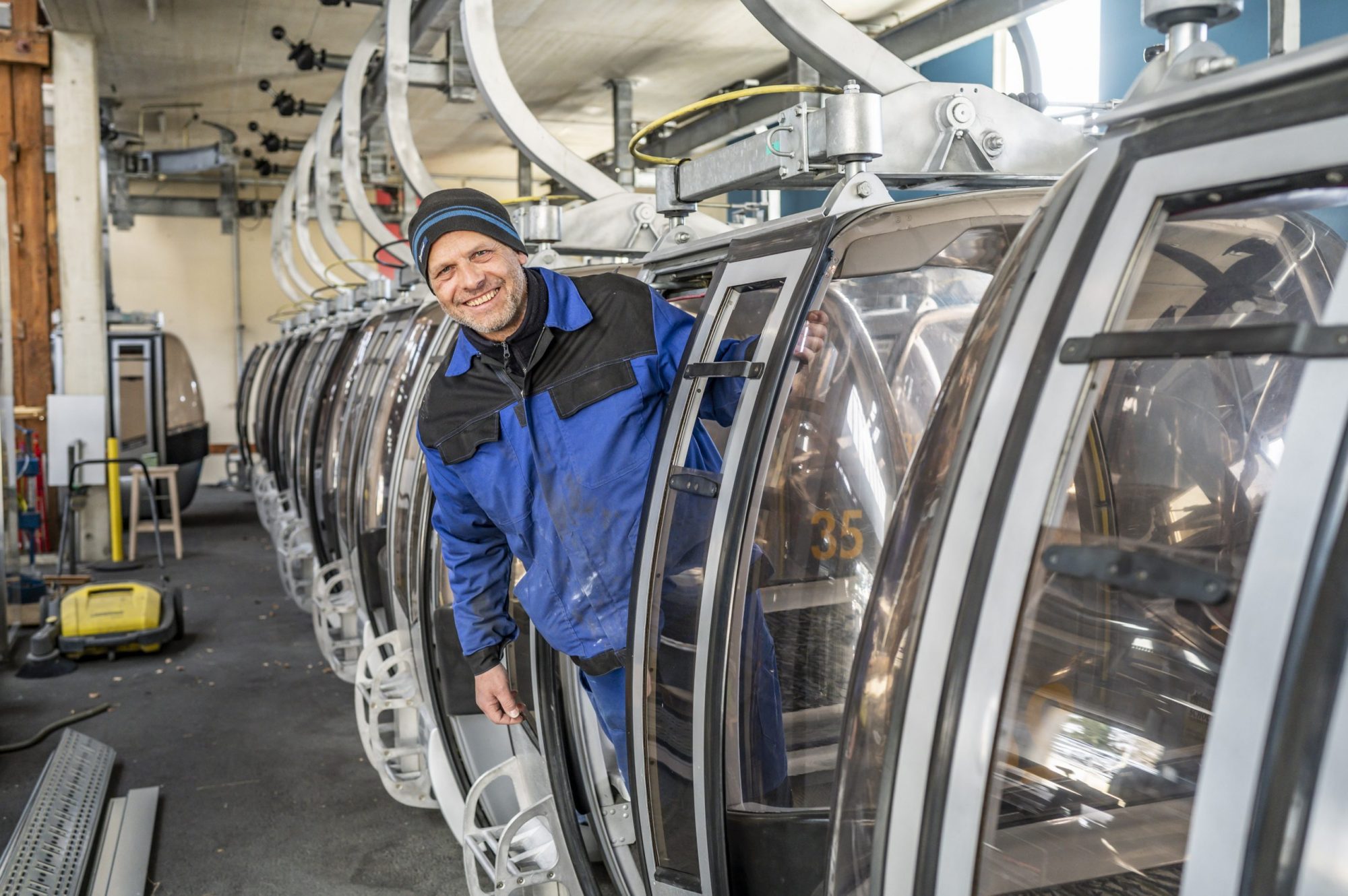Ein Mitarbeiter in blauer Arbeitskleidung lächelt aus Gondel der Schöckl-Seilbahnstation.
