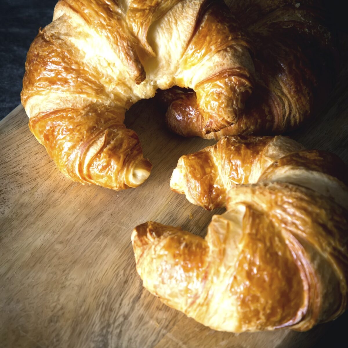 Frische, goldbraune Croissants auf einem Holzbrett, ideal für Frühstück oder Kaffeezeit.