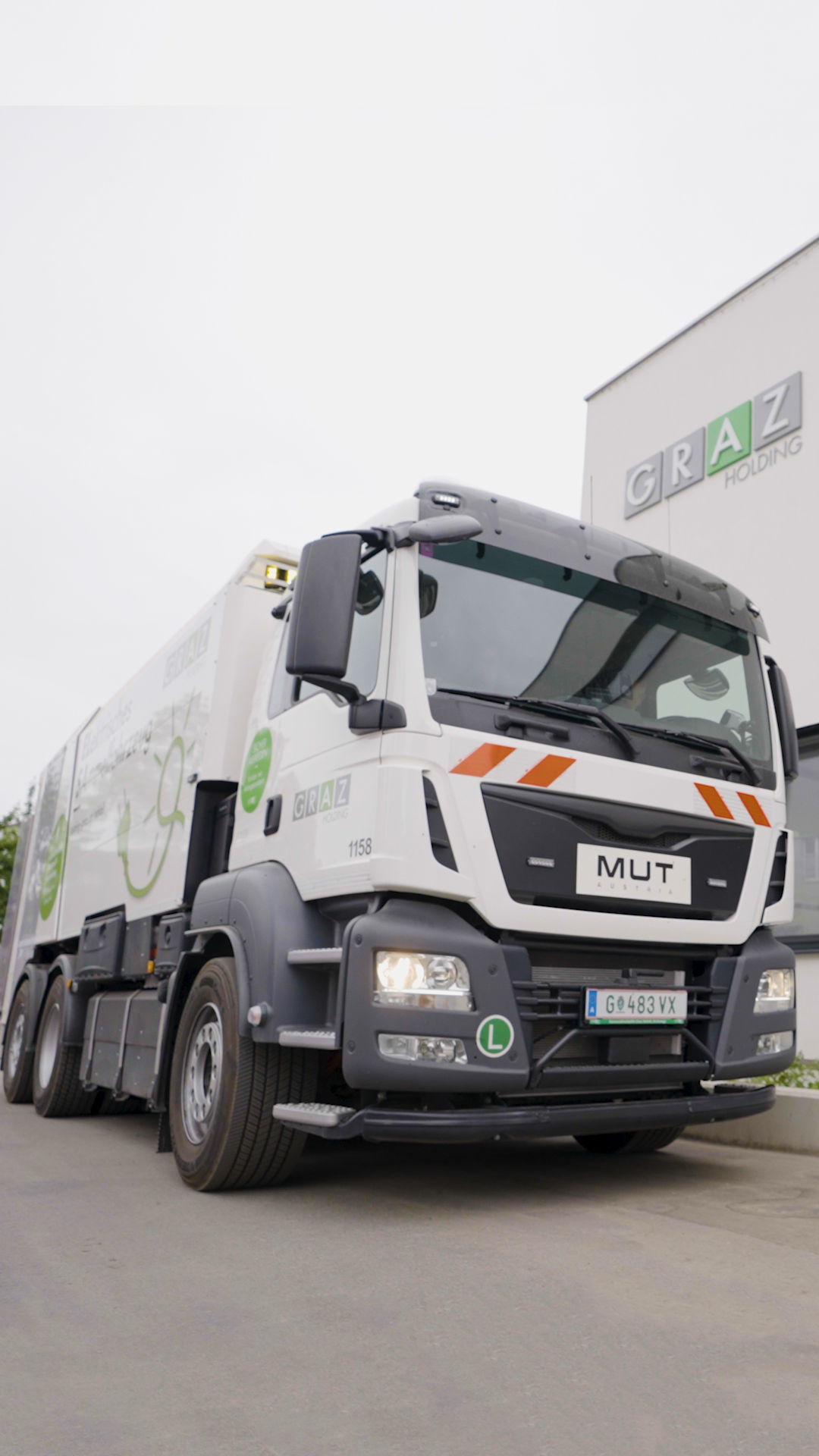 Vorderansicht eines Müllfahrzeugs der Holding Graz, geparkt vor Gebäude mit Firmenlogo.