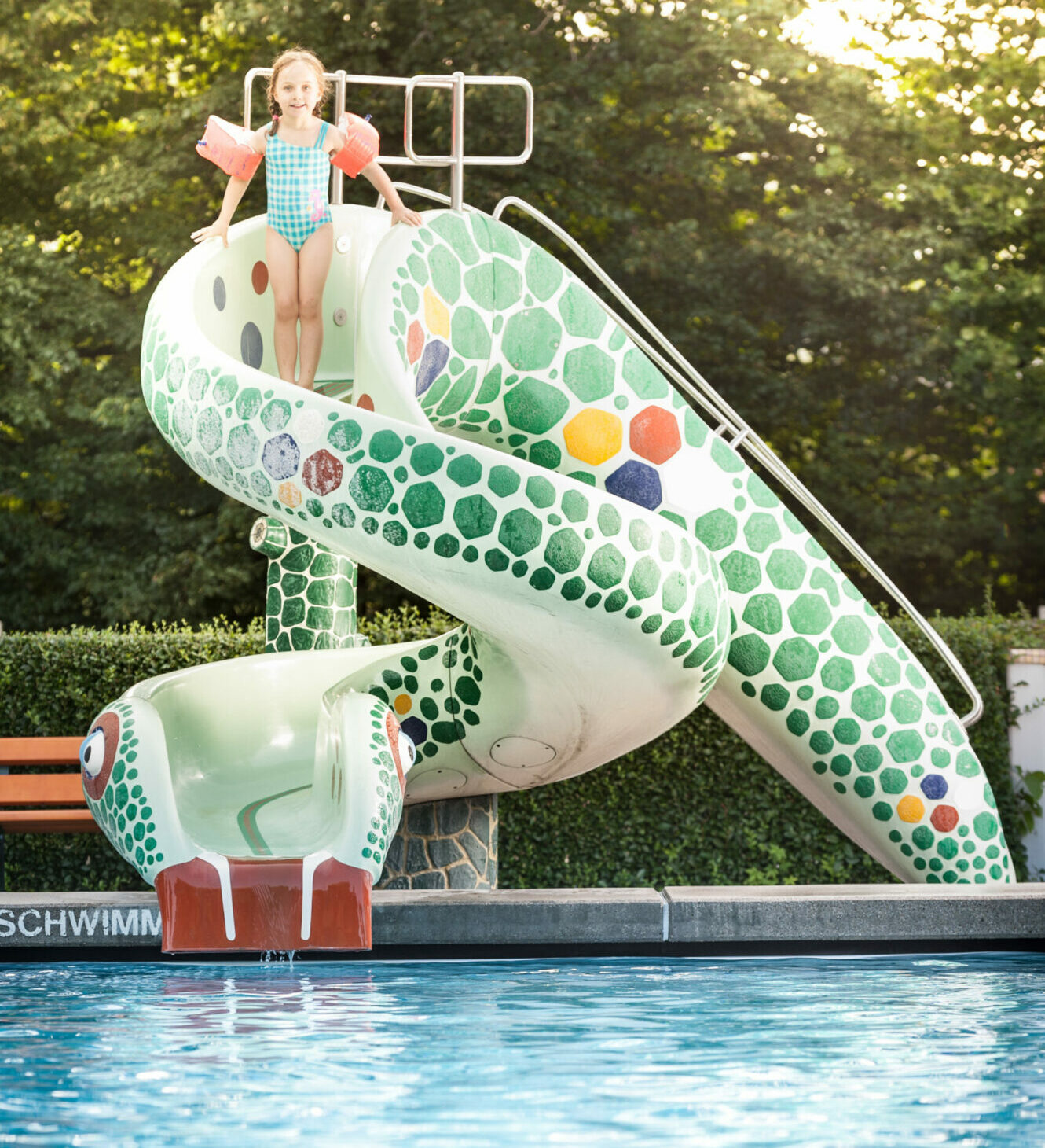 Kind mit Schwimmflügeln auf grün gemusterten Rutsche Schlangenform im Stukitzbad.